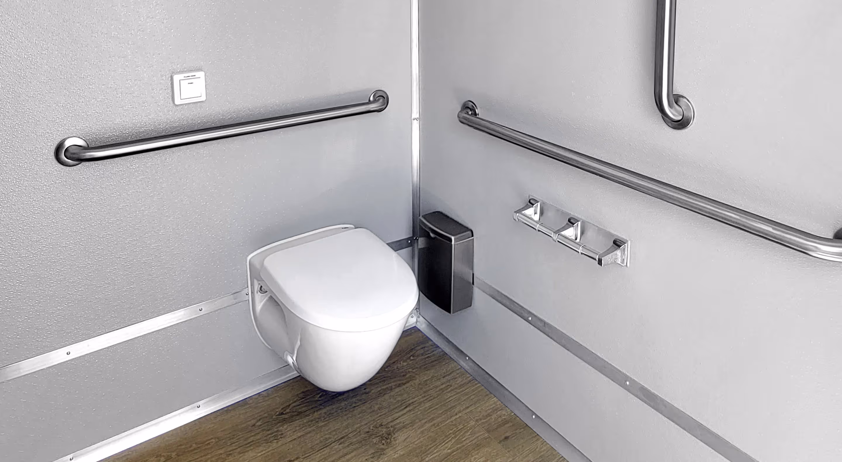 Accessible bathroom corner with wall-mounted toilet and stainless steel grab bars on gray walls.