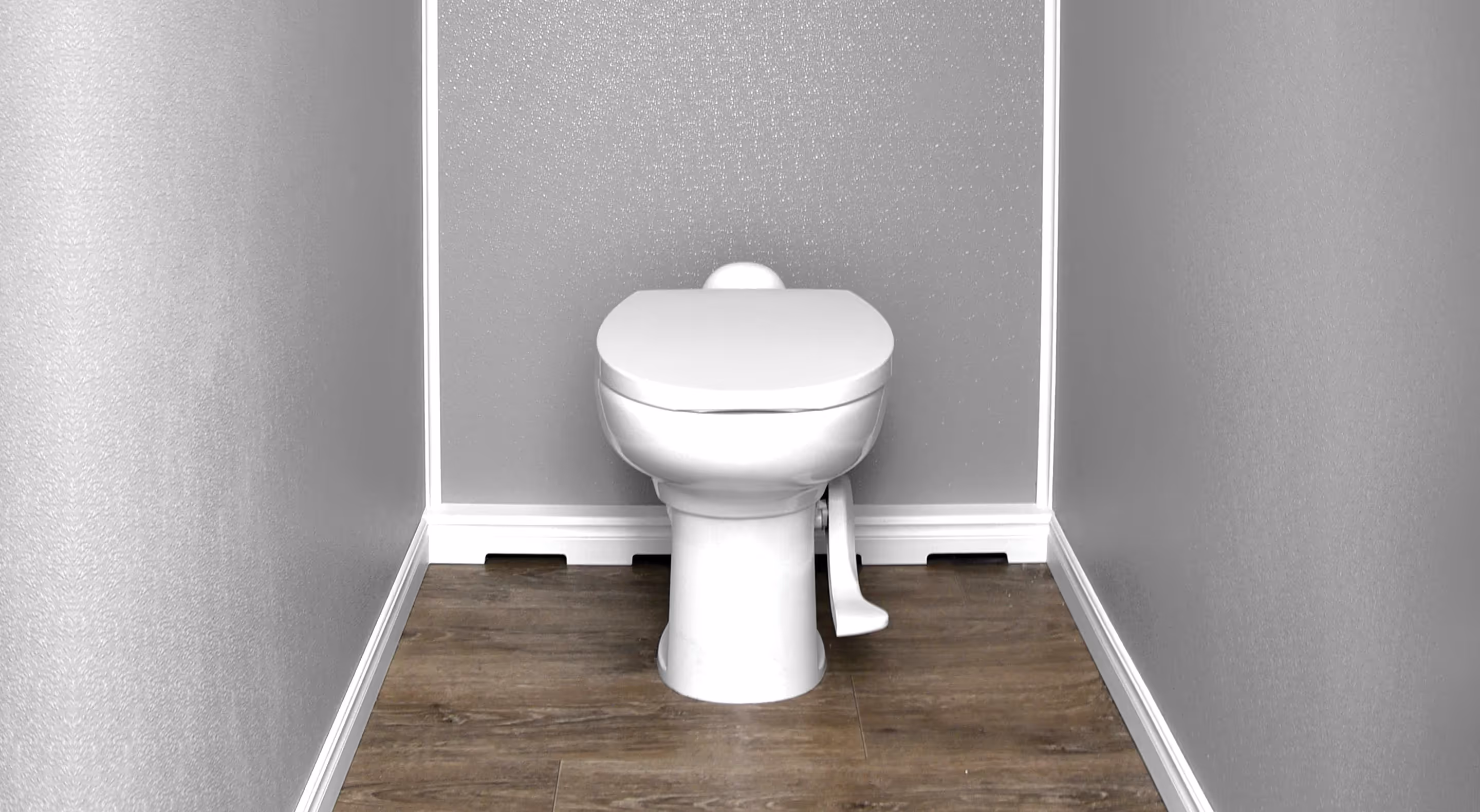 White toilet with a foot pedal flush mechanism against a gray wall and wood floor.