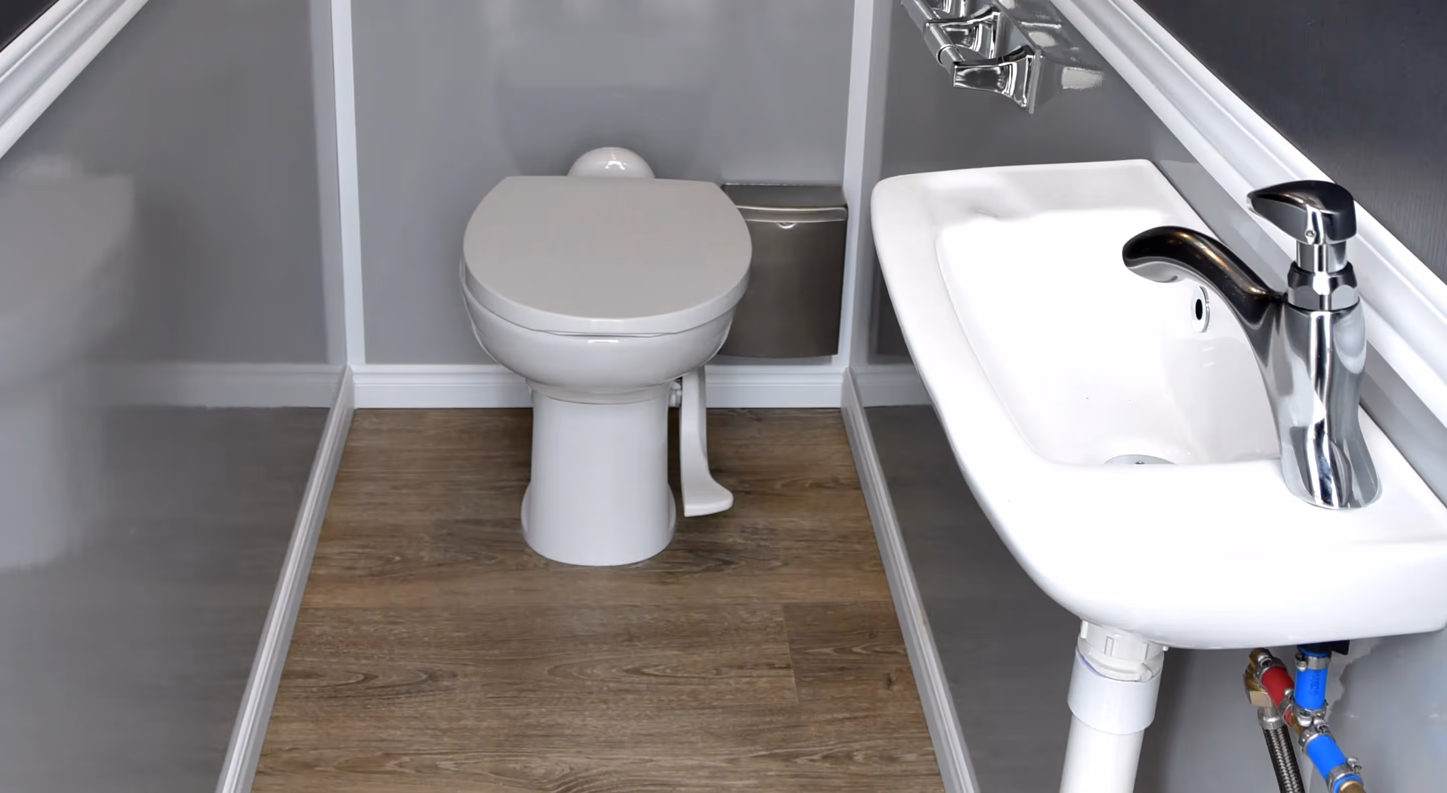 Compact bathroom with white toilet, sink with chrome faucet, and wood-look floor.