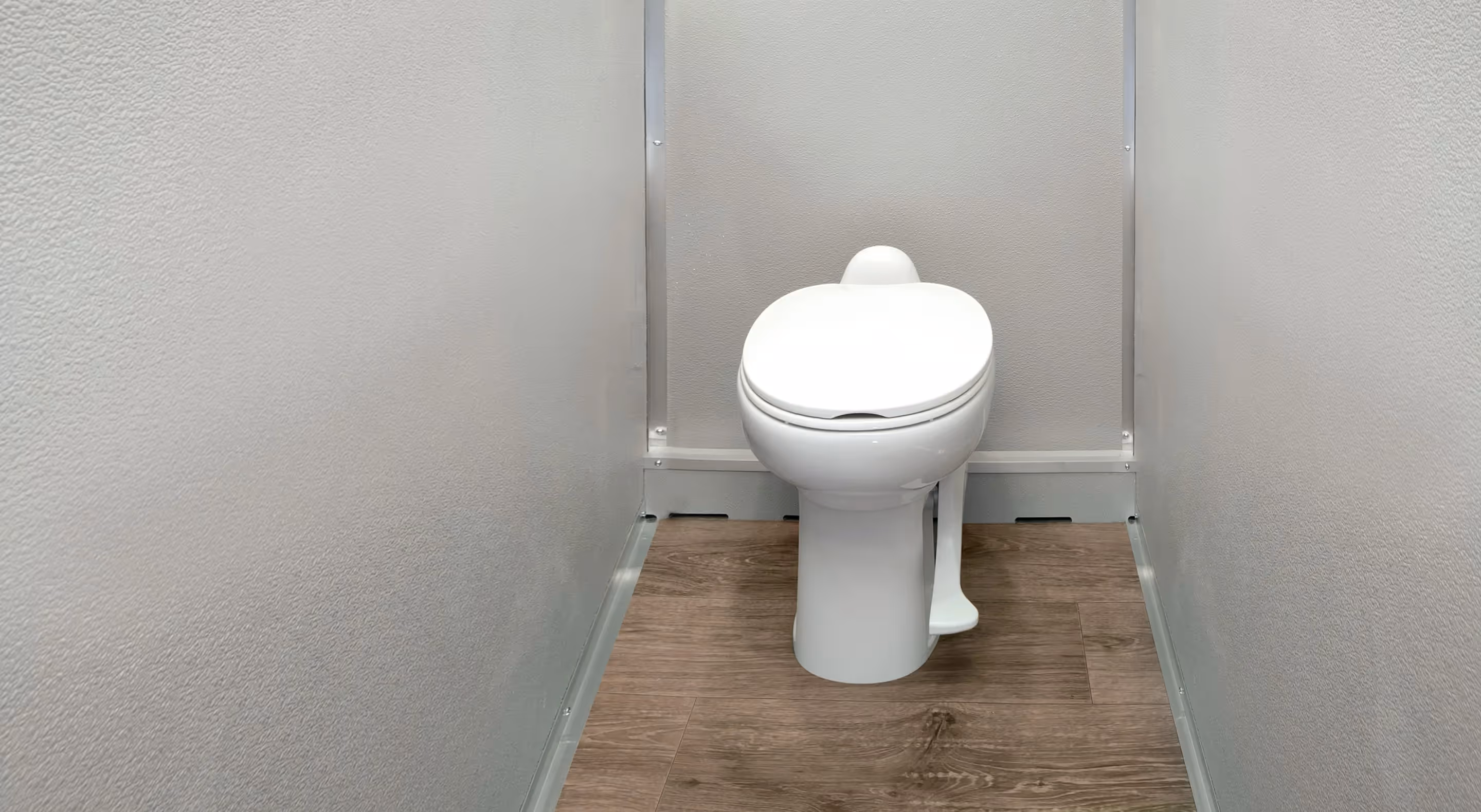 Compact white toilet with a pedal flush in a small room with wood-look flooring and gray walls.