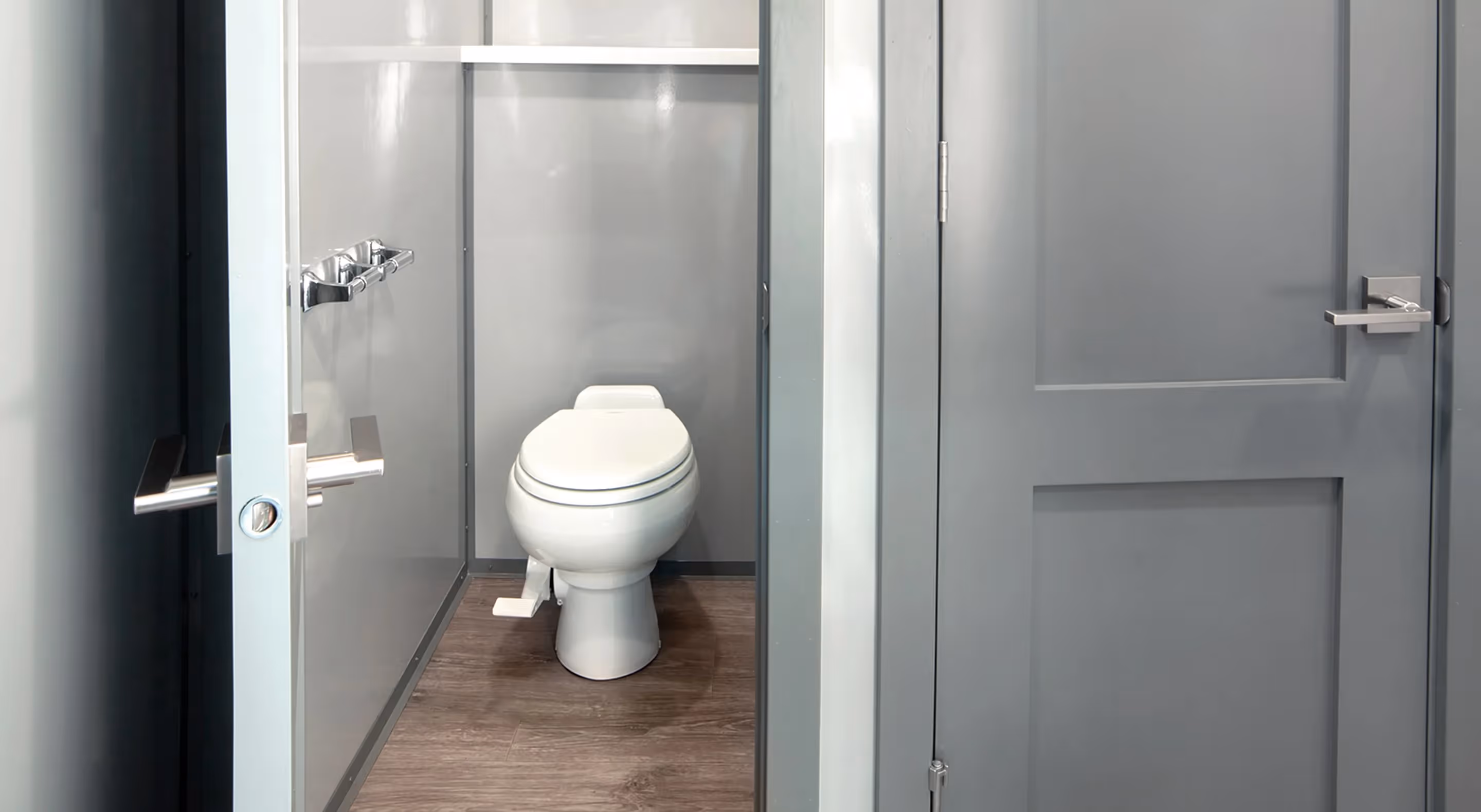 Modern small bathroom stall with closed white toilet and gray metal walls and door.