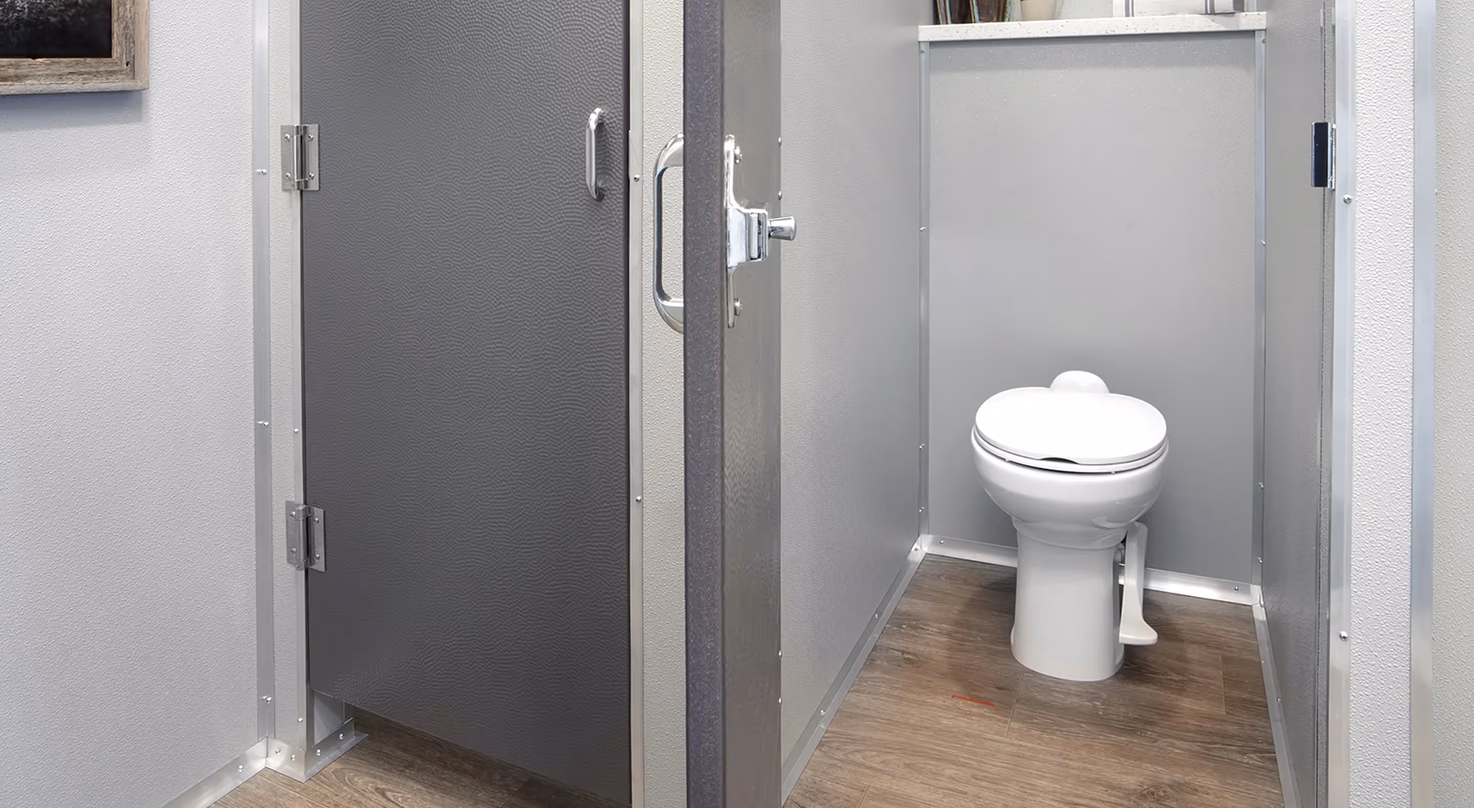 Interior view of a clean commercial restroom stall with a white toilet and wood-look flooring.