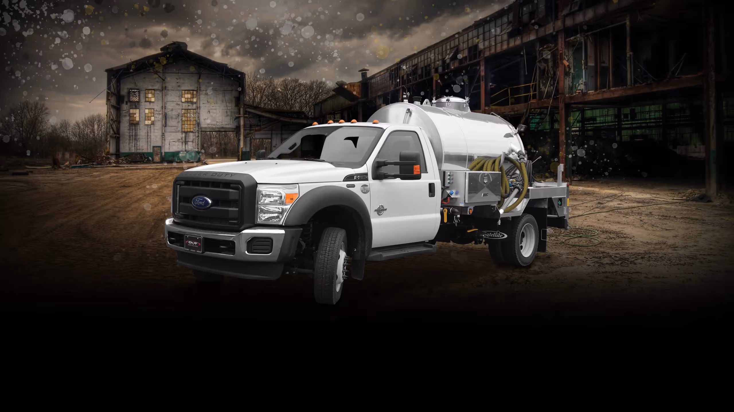 White Ford F-750 truck with a water tank, set against a dilapidated industrial background.