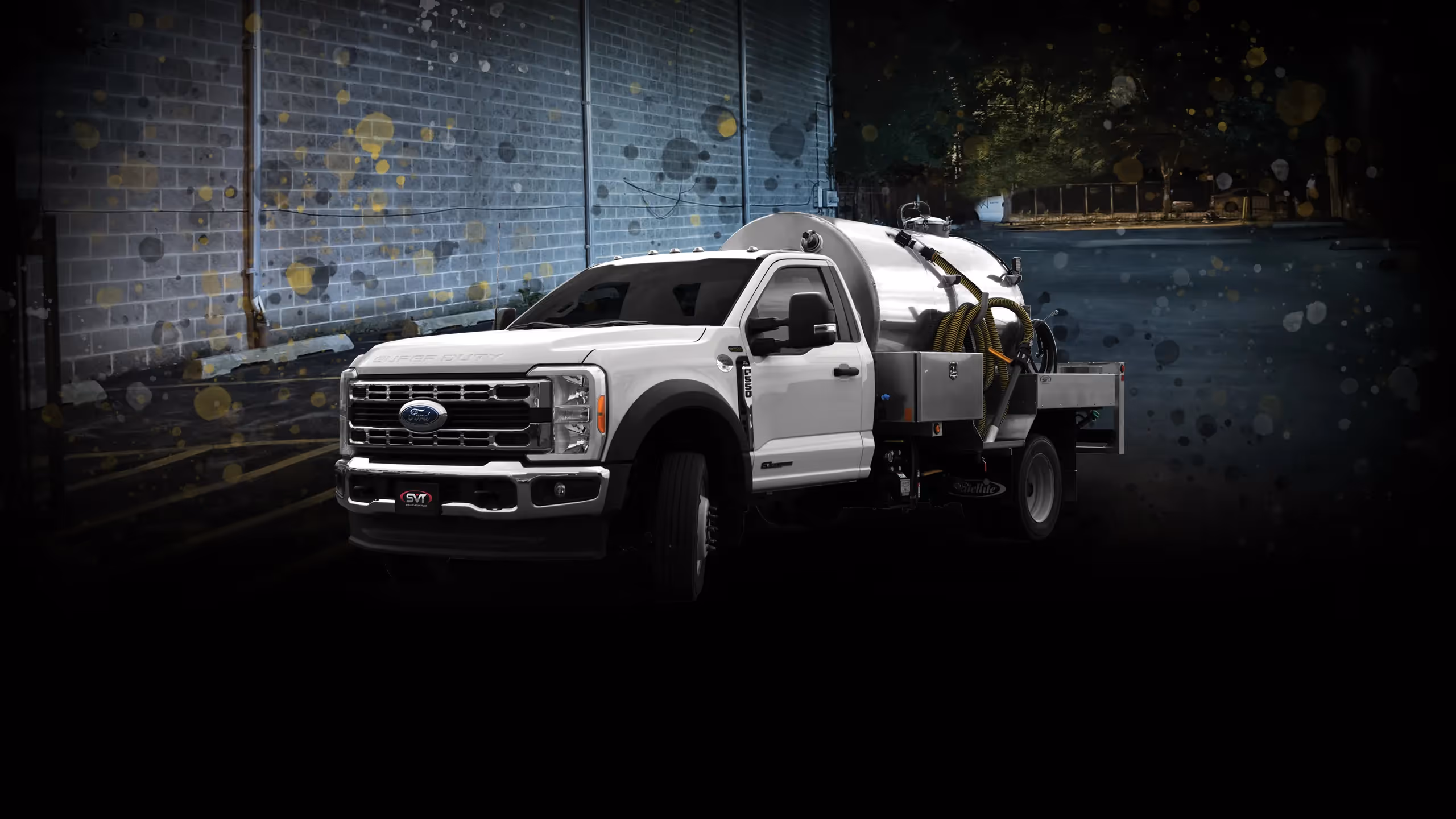 A white Ford F-450 truck with a tank and equipment on a dark industrial background.