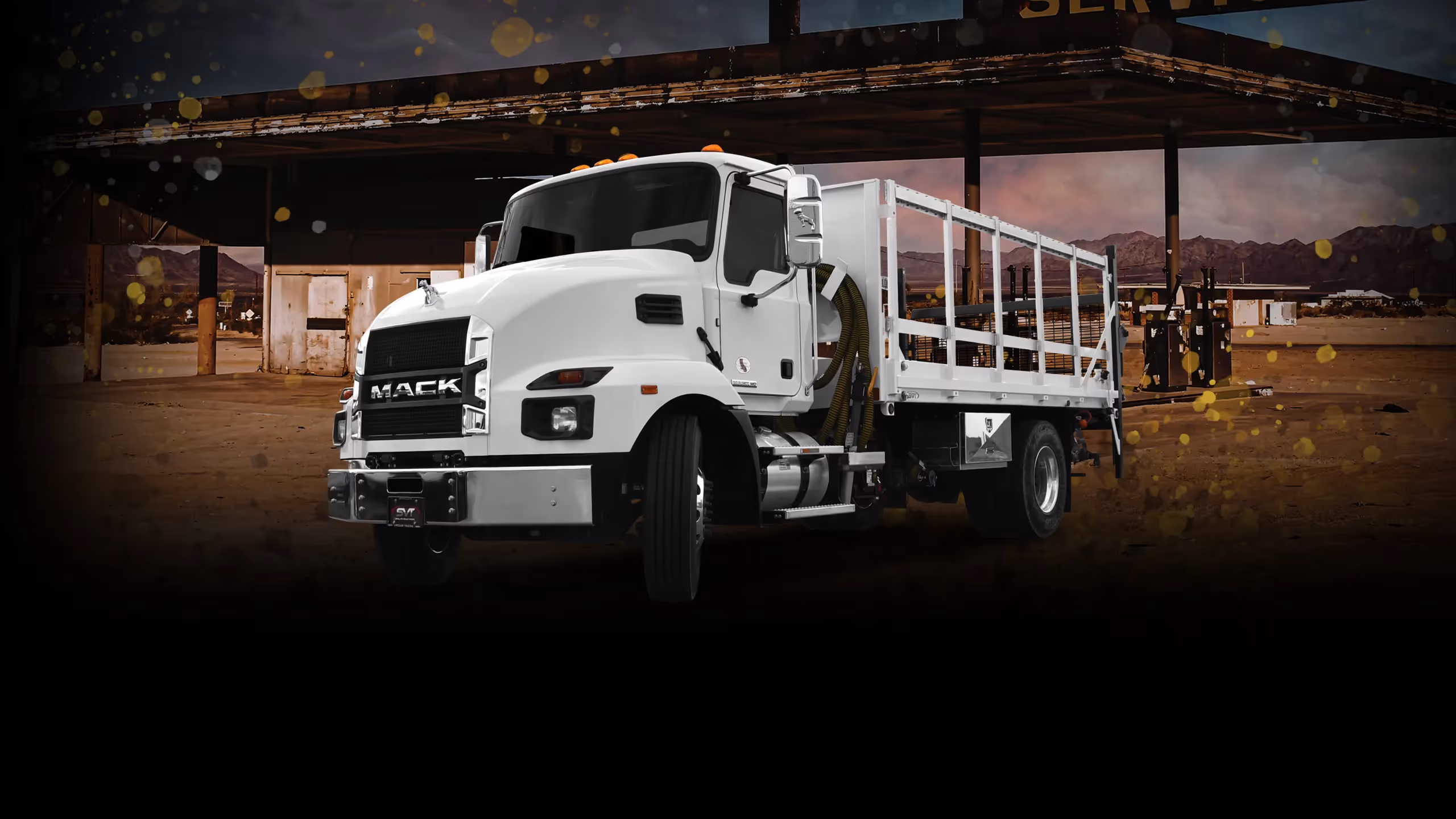 White Mack truck with a flatbed, parked in a rustic service station setting.