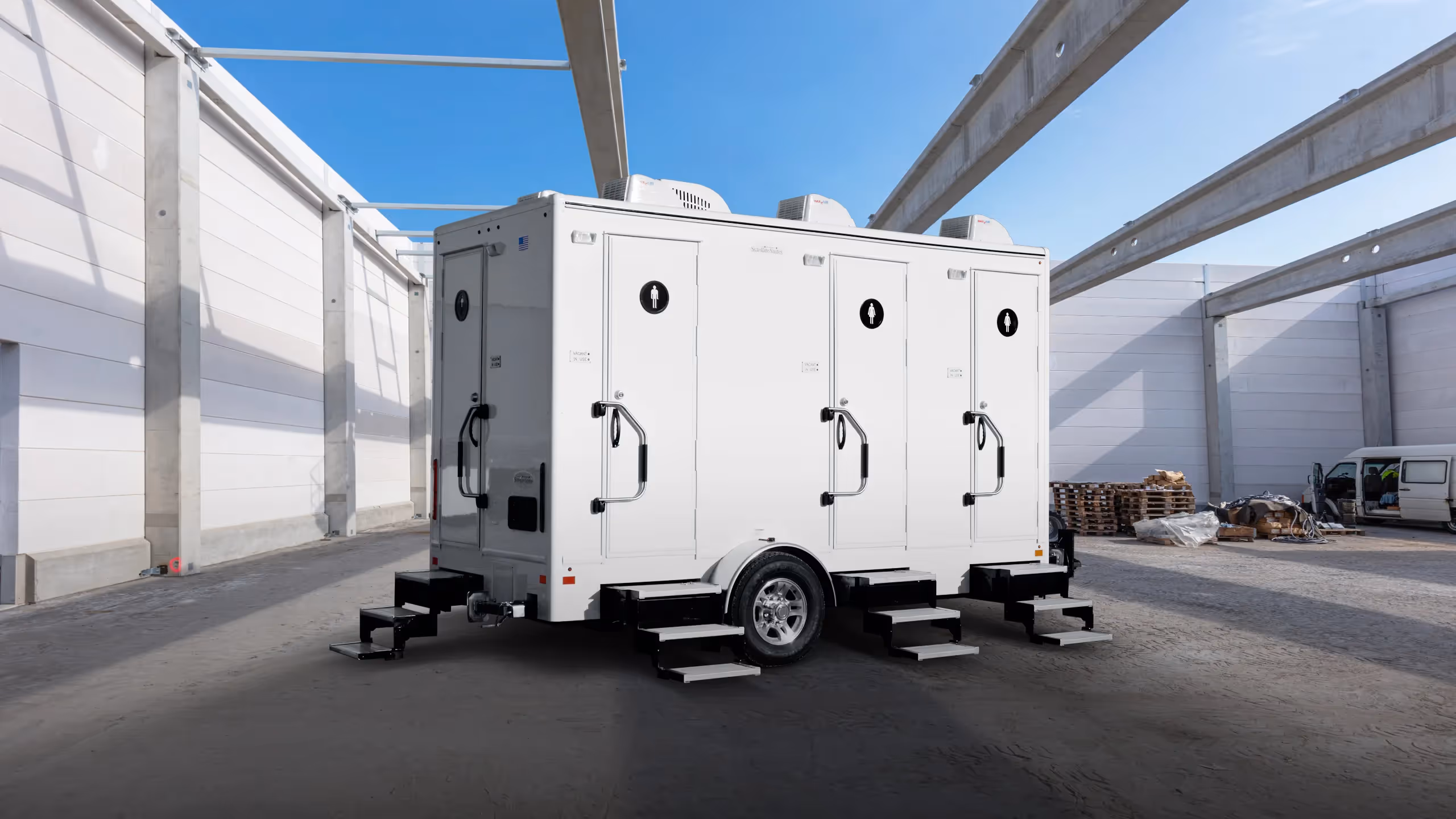 Mobile restroom trailer with four doors, four stations, and steps, set in an industrial space.