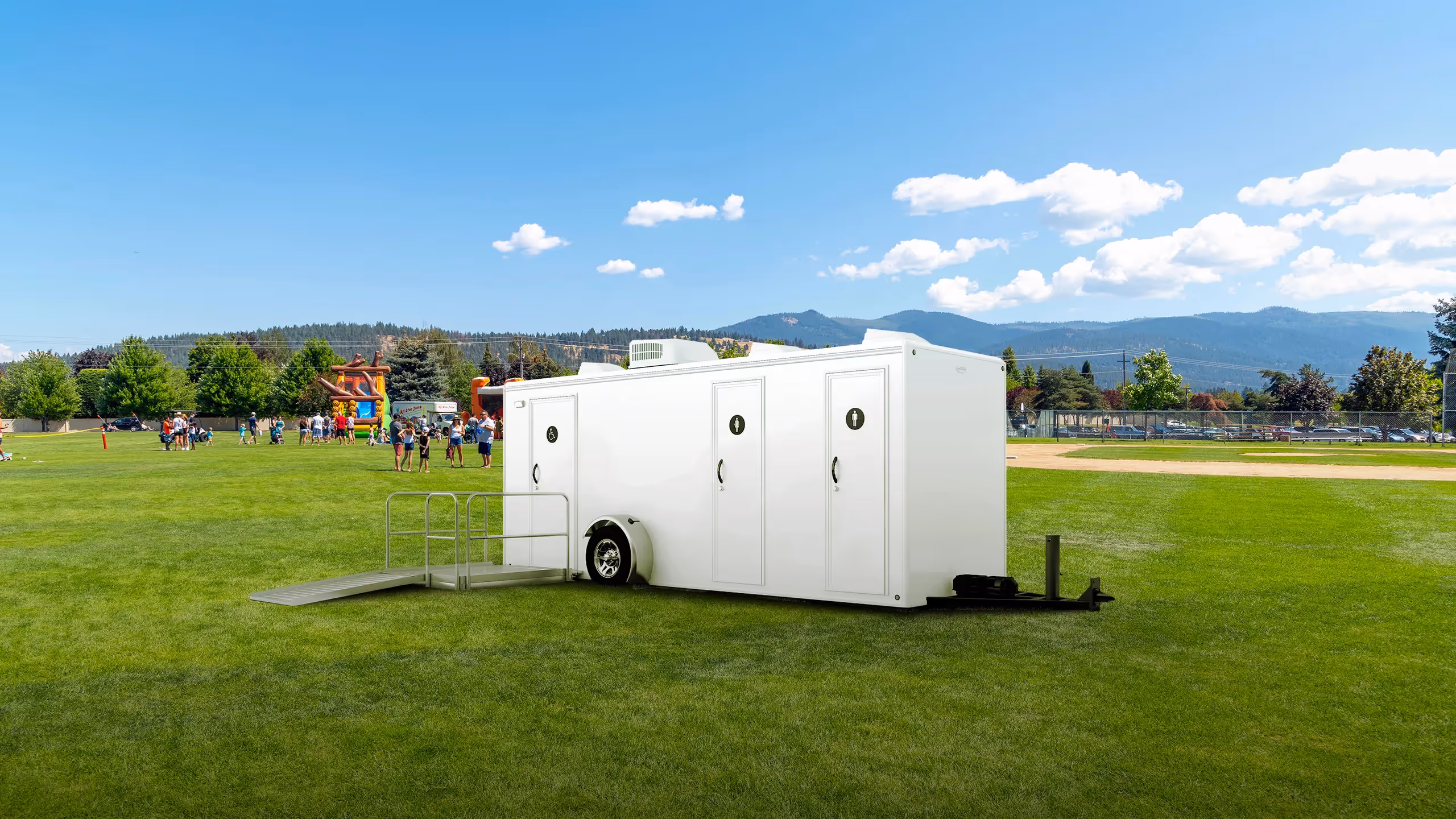 ADA-compliant mobile restroom trailer with three doors and a ramp, placed on a grassy field.