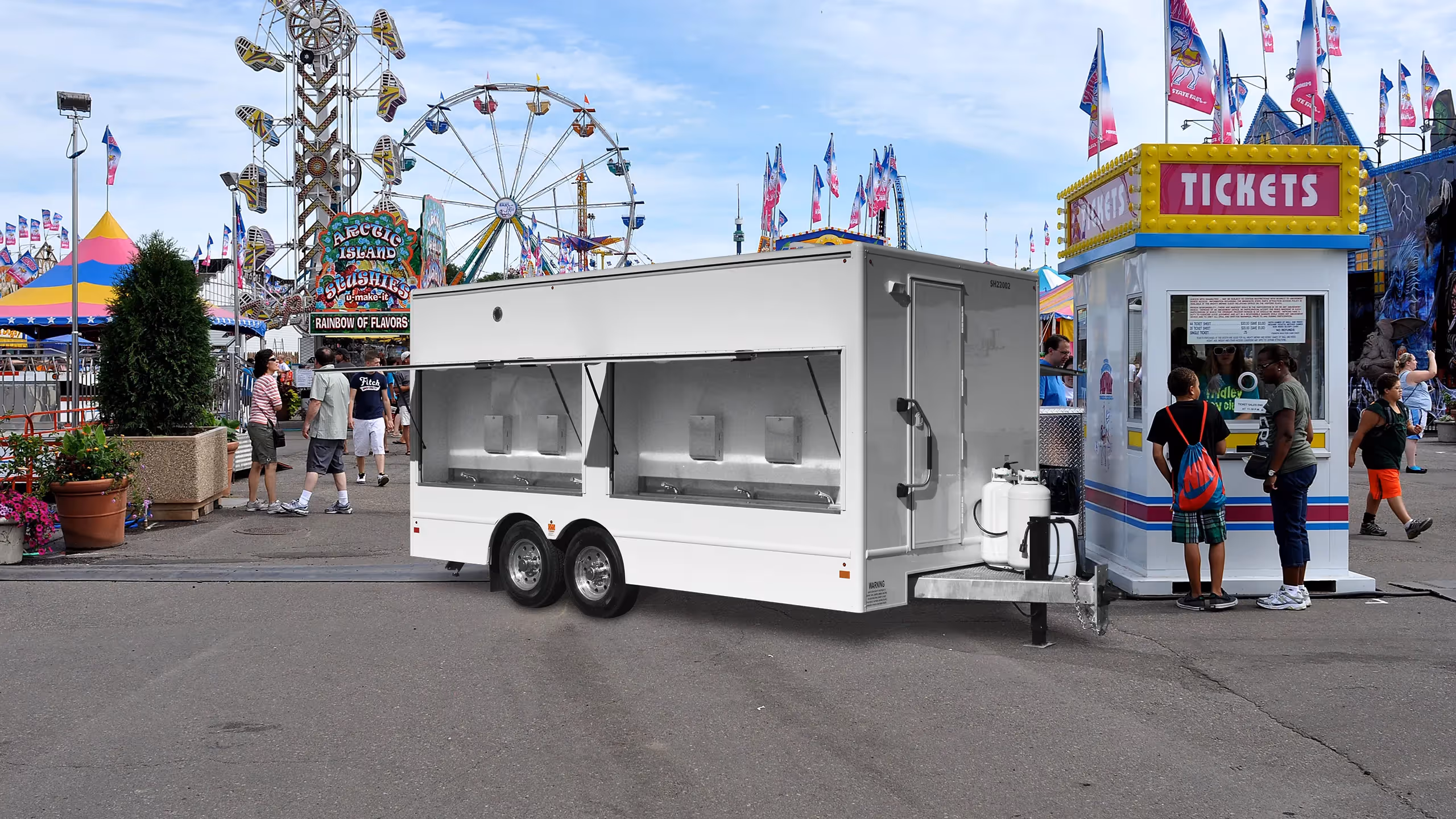 A large, white mobile food trailer with sinks, parked at a fairground with colorful booths and