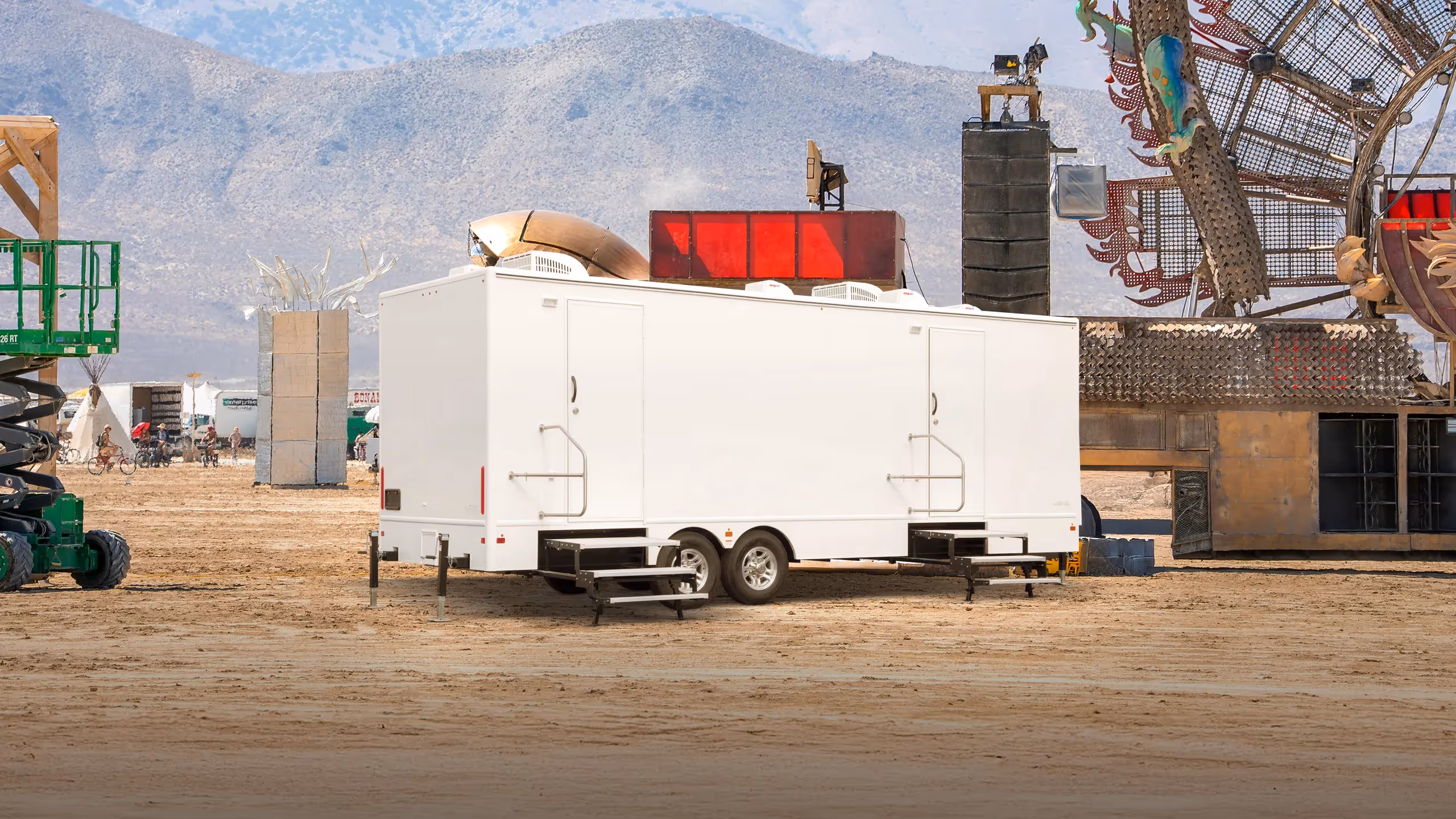 A white 9-station restroom trailer is parked on a desert landscape near art installations.