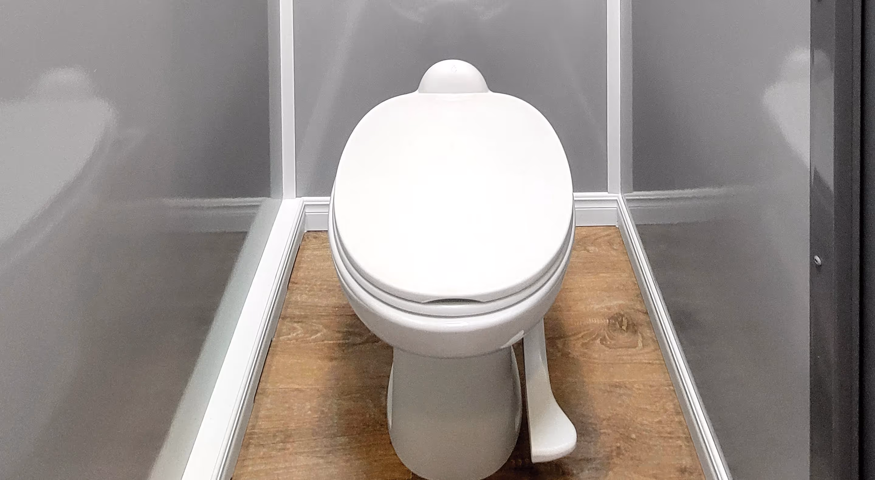 A white toilet in a compact, gray-walled restroom with a wooden floor.