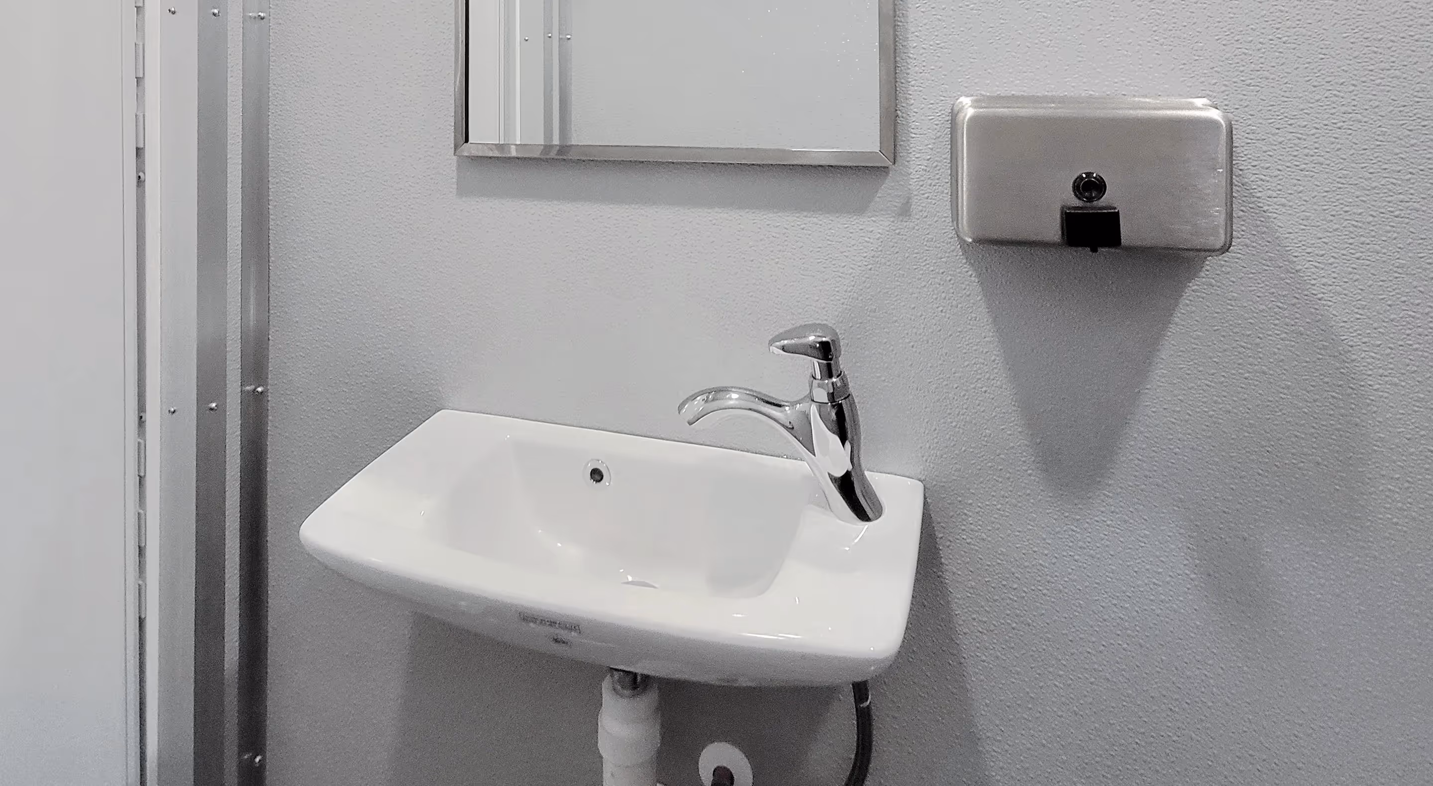 Compact restroom interior featuring a wall-mounted sink, mirror, and soap dispenser.
