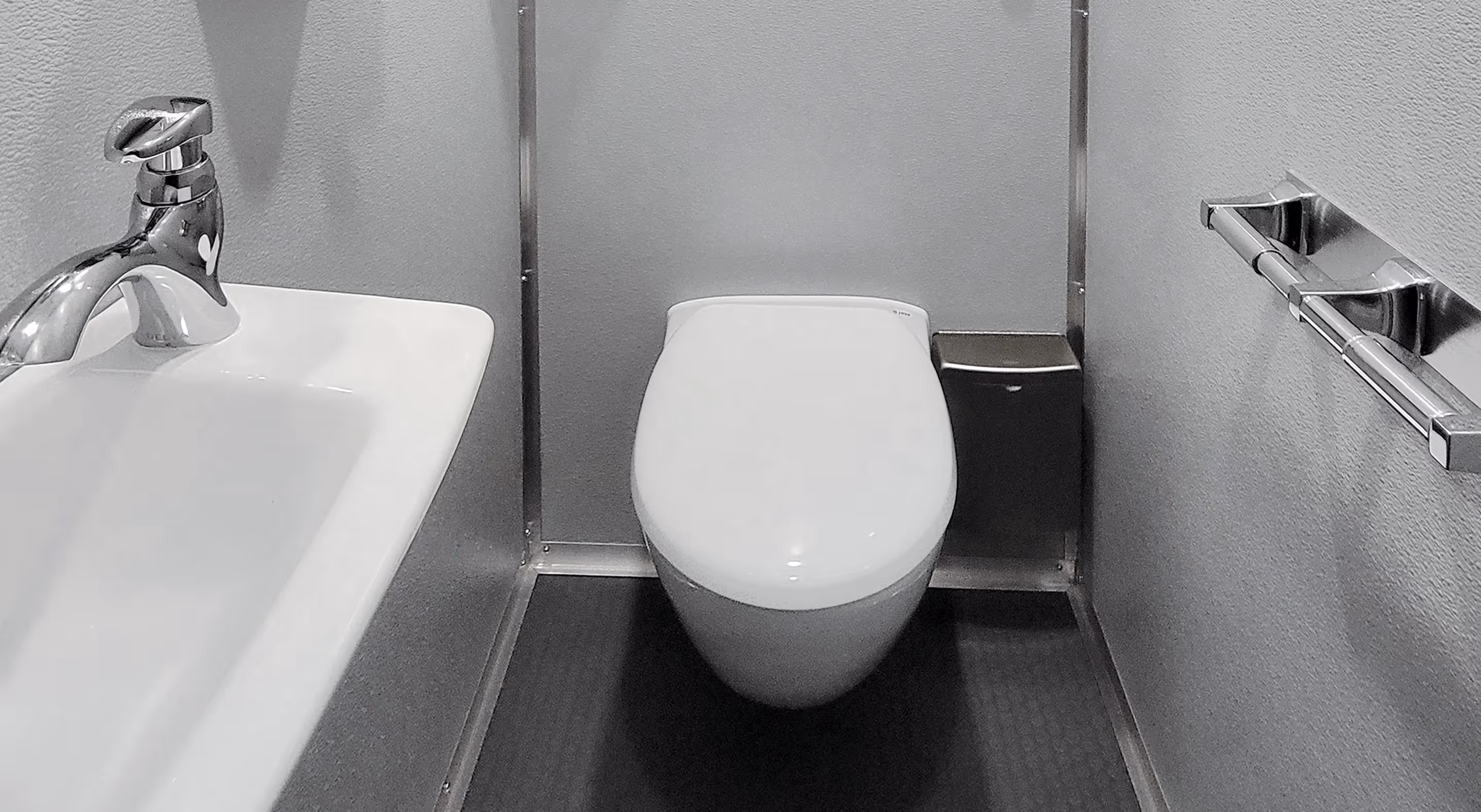 Compact restroom interior featuring a modern toilet, sink, and steel handrail.
