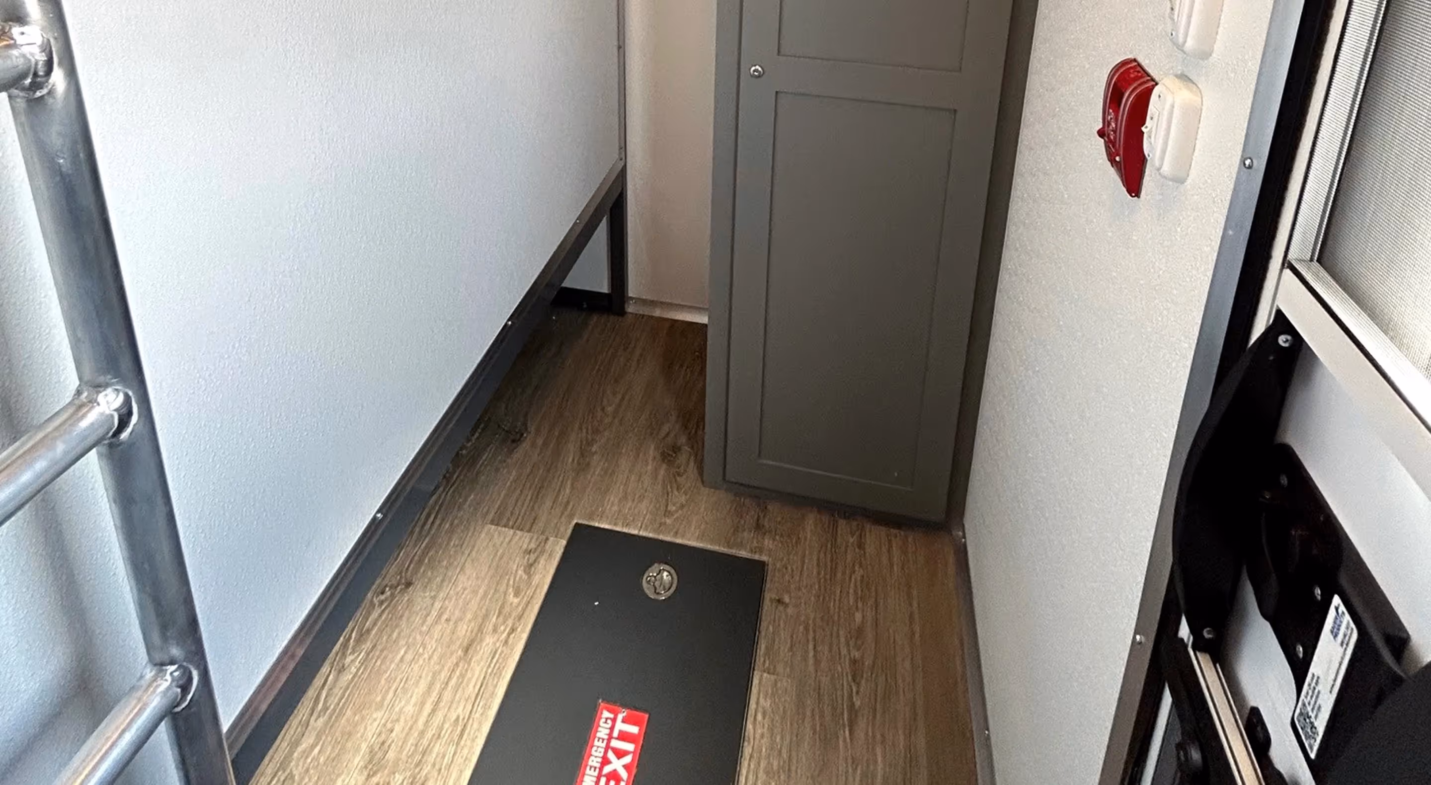 Interior of a compact sleeping area featuring a ladder, storage cabinet, and a floor mat.