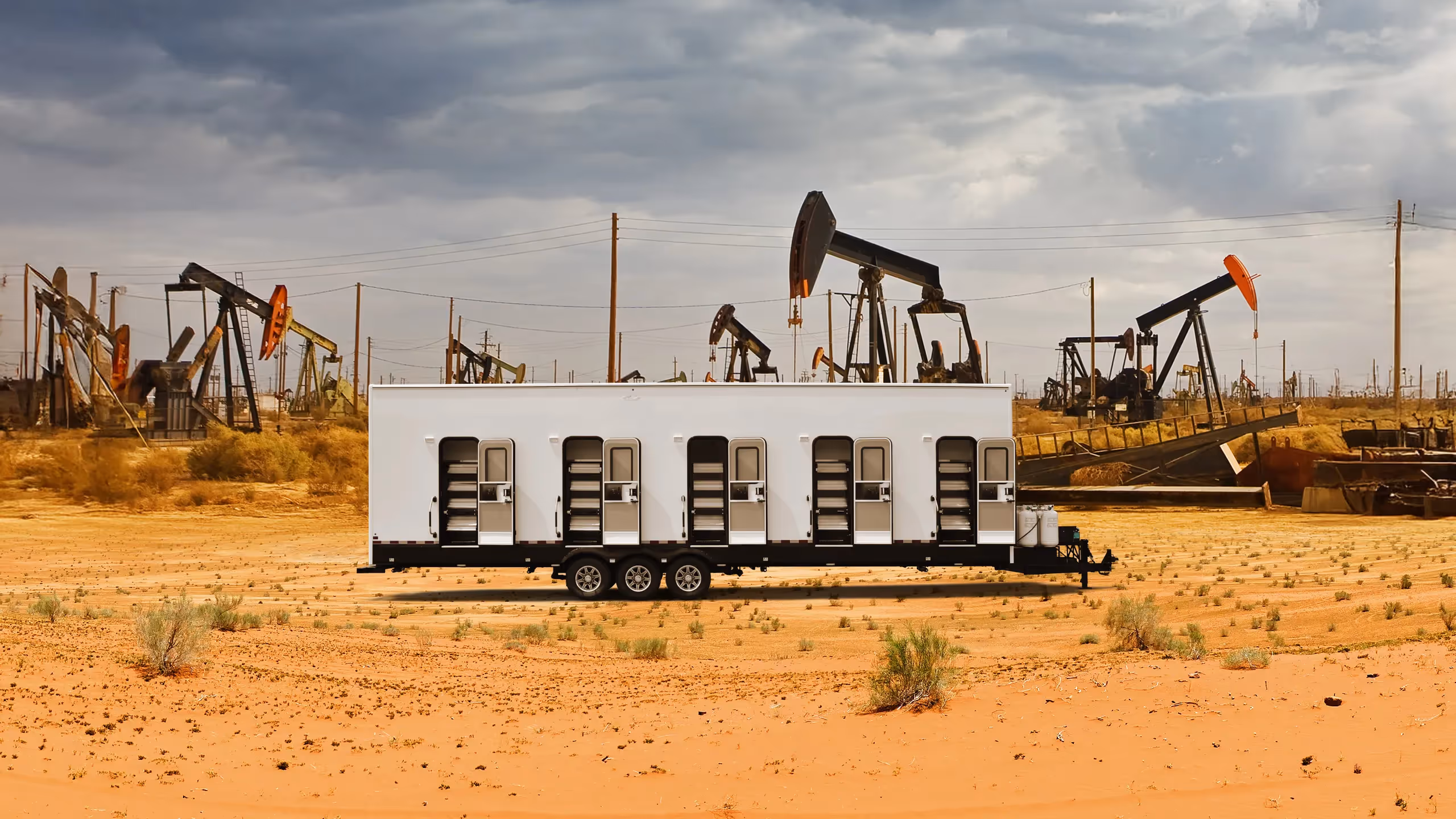 A white trailer with multiple doors stands in a desert landscape near oil pump jacks.