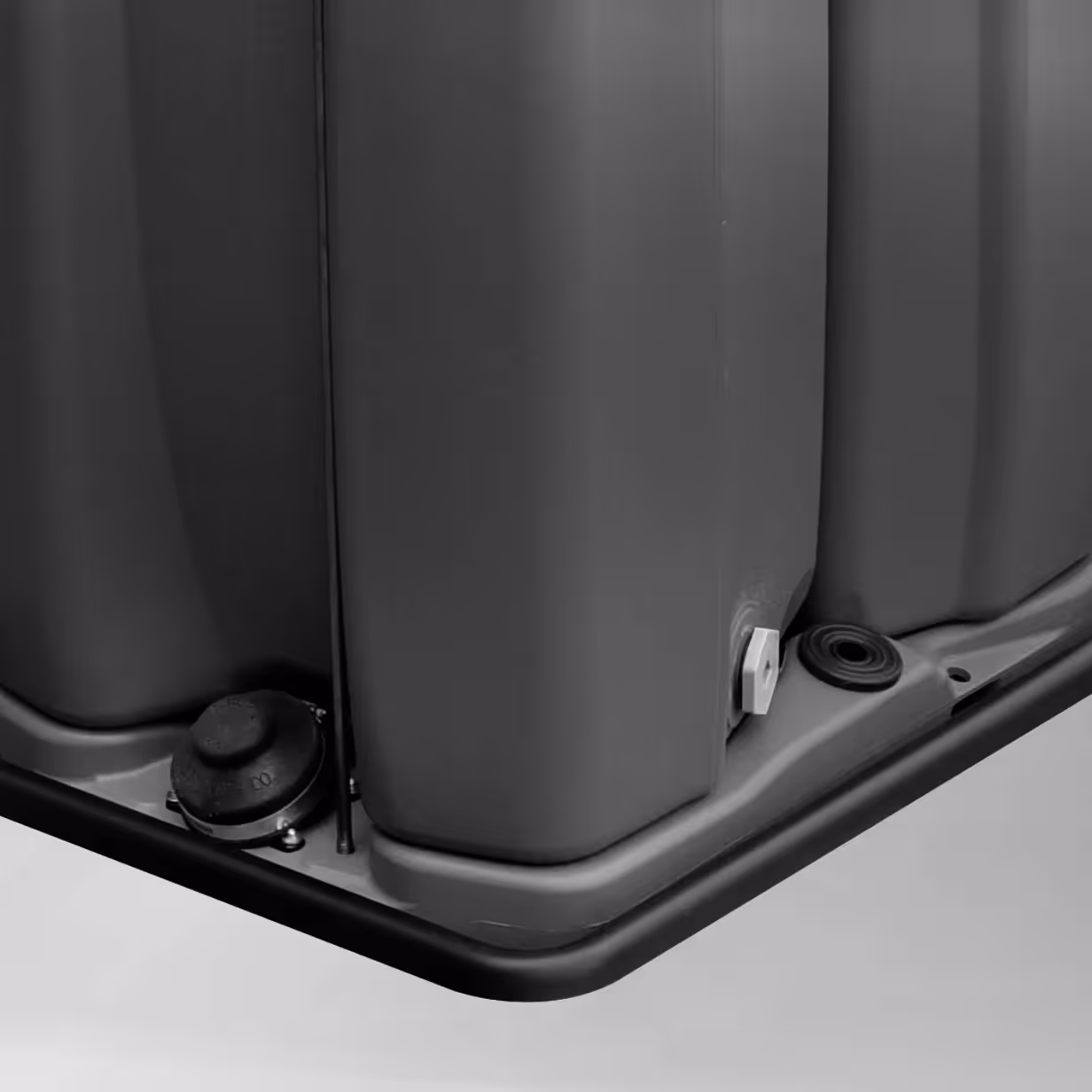 Close-up of a gray containment tray corner with plugs and a bolt on a smooth surface.