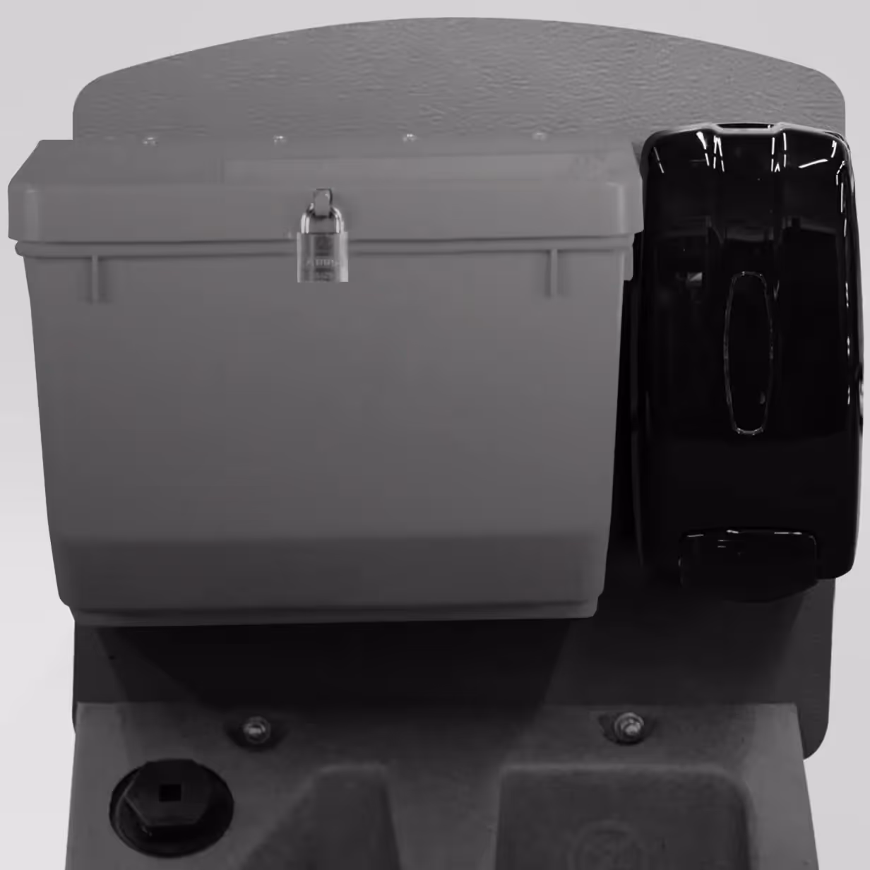 Wall-mounted board with a locked gray plastic box and a black dispenser attached side by side.