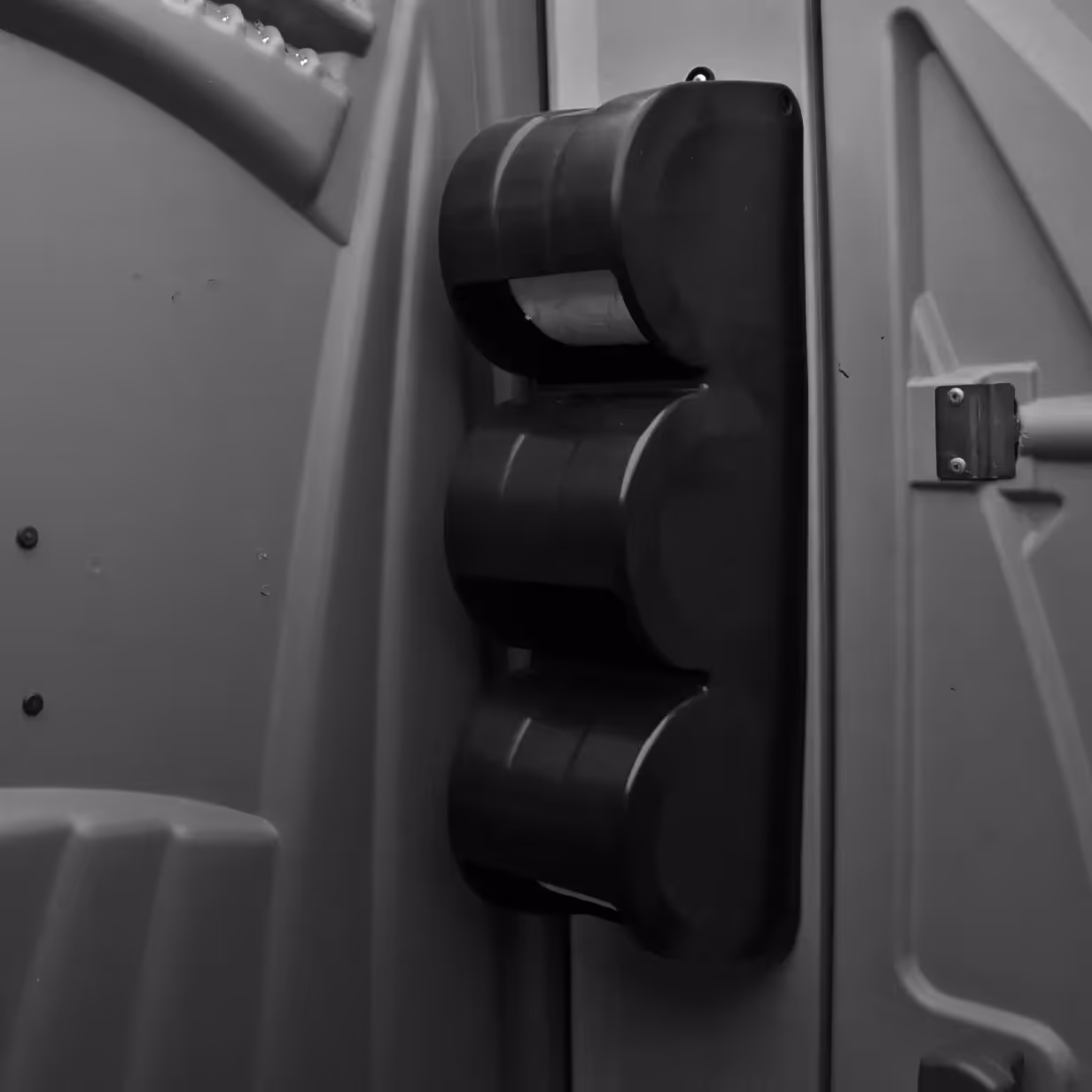 Black triple-roll toilet paper holder mounted inside a portable toilet stall.