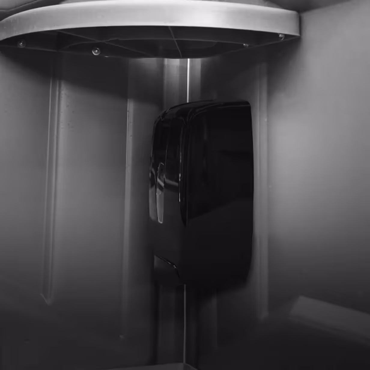 Black automatic soap or sanitizer dispenser mounted inside a grey plastic enclosure.