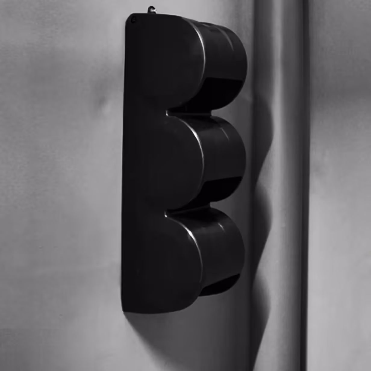 Black vertical traffic light housing with three round sections mounted on a gray wall.