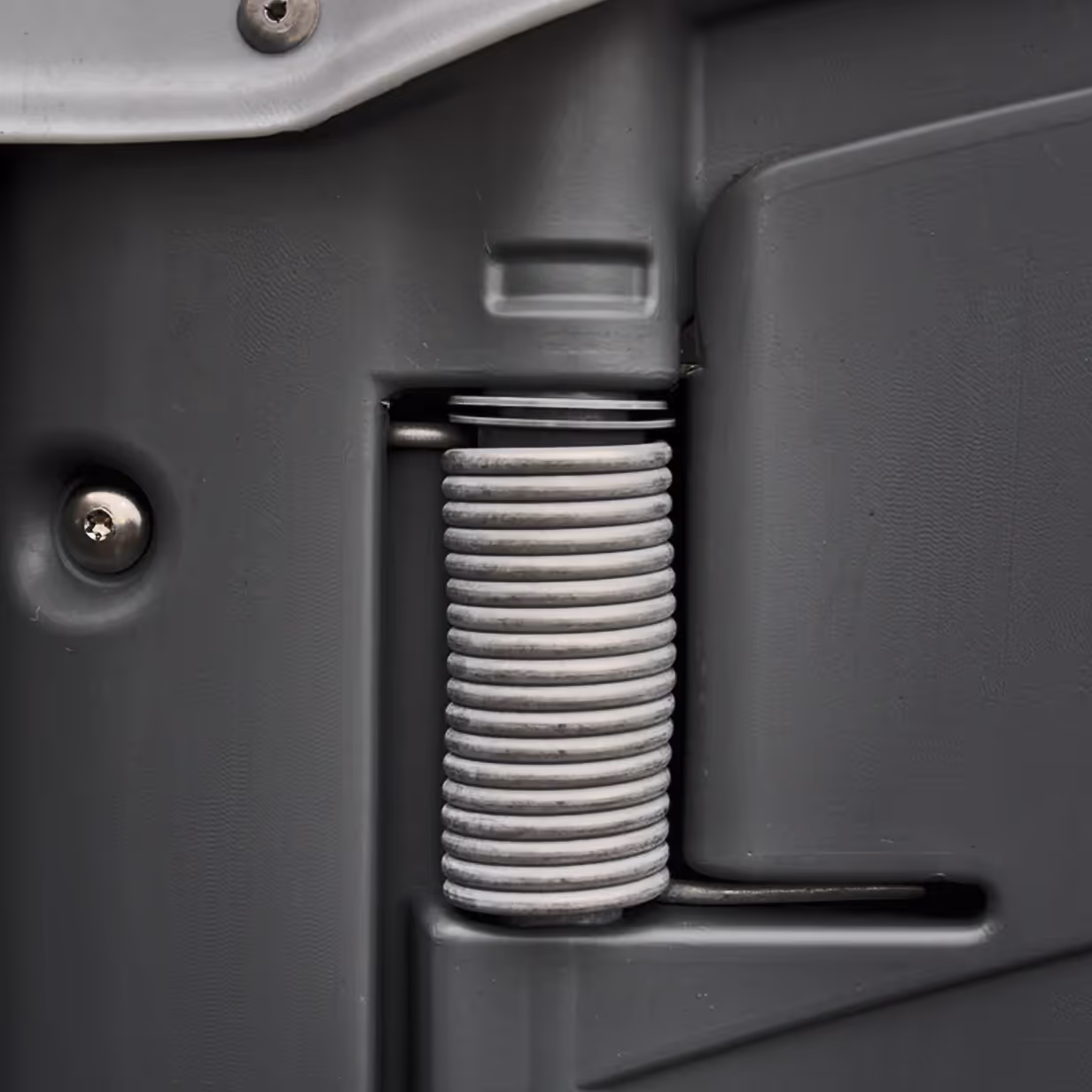 Close-up of a metal door spring encased in a gray plastic housing with visible screws.