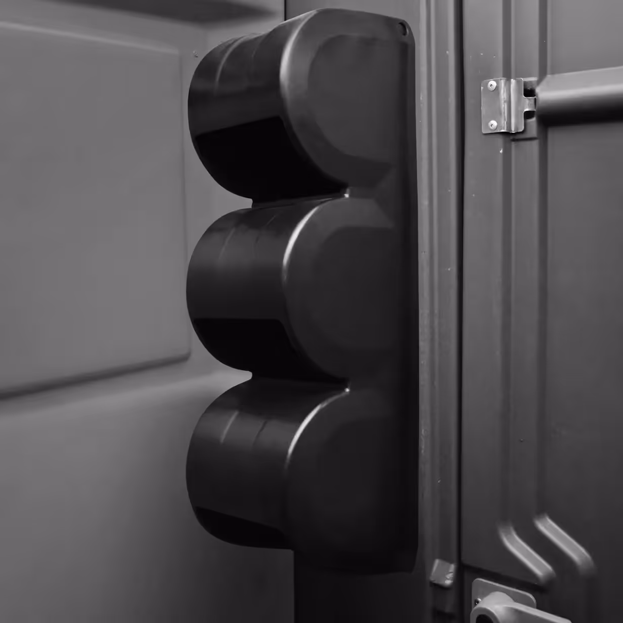 Black triple roll toilet paper holder mounted inside a gray portable toilet stall.