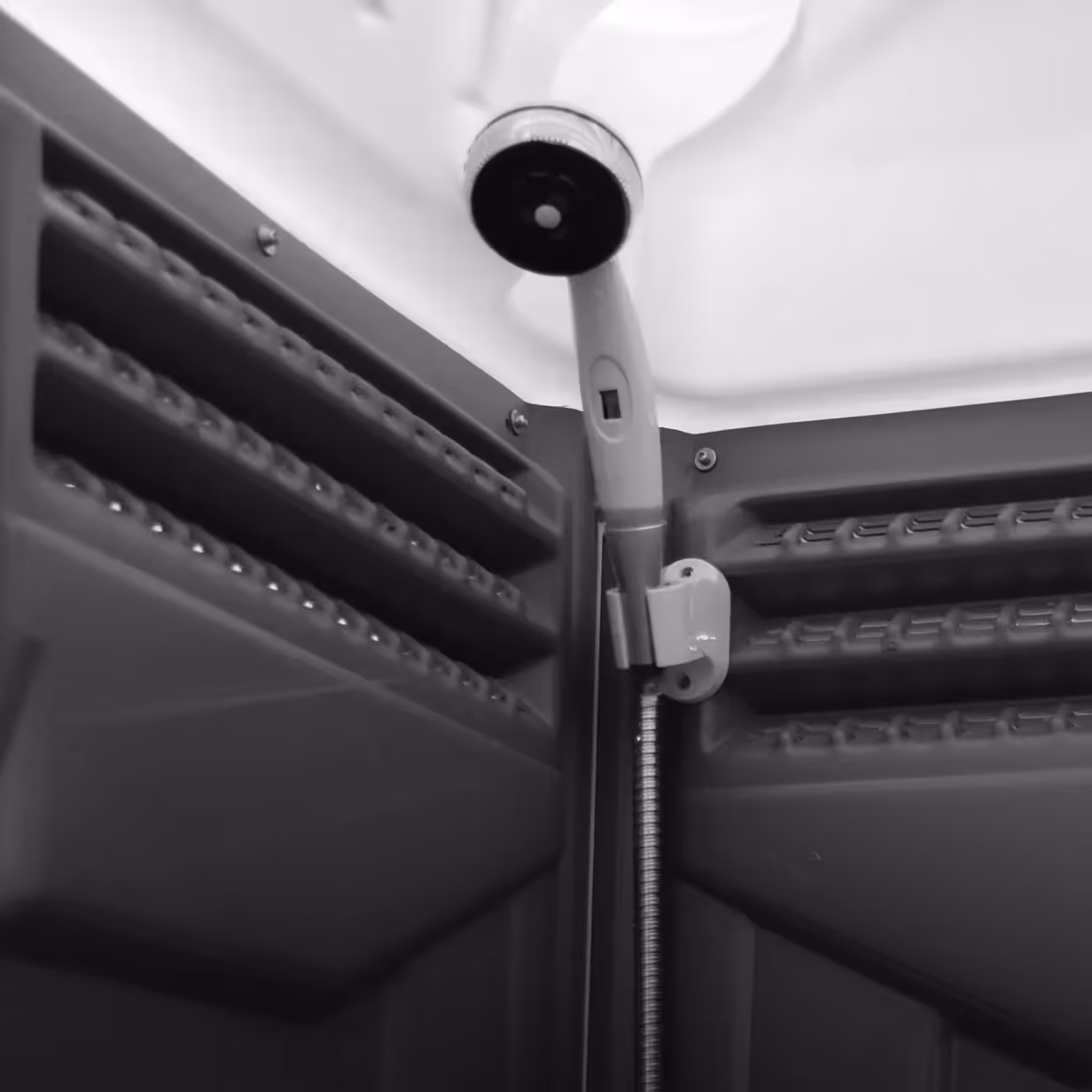White handheld showerhead mounted inside a dark textured shower enclosure corner.