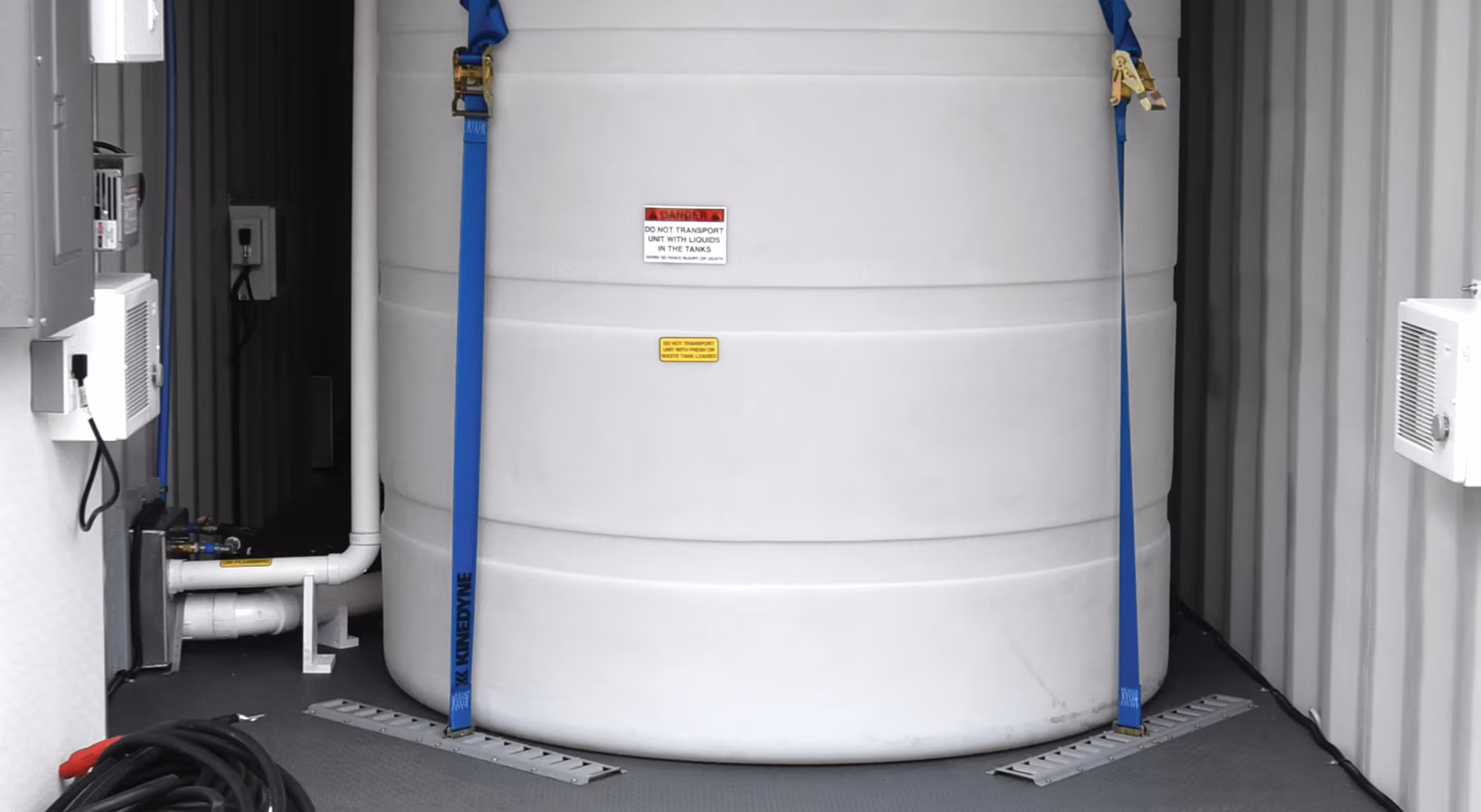 Large white tank secured with blue straps inside a shipping container, featuring piping and