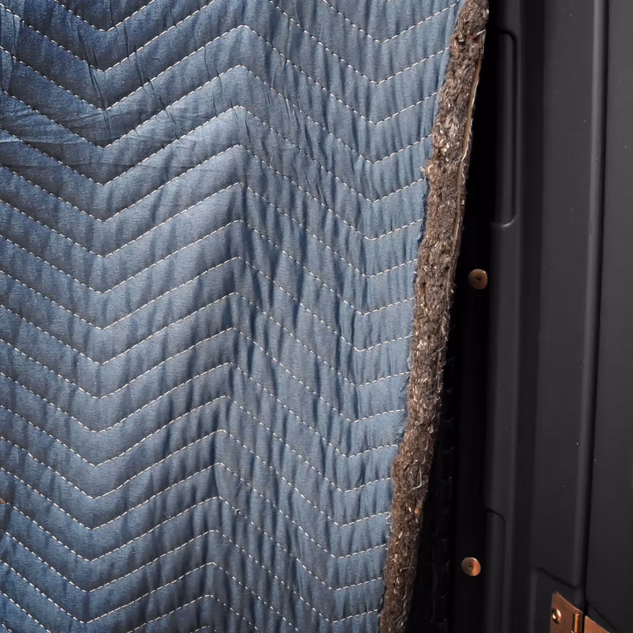 Quilted blue fabric with chevron stitching and a rough textured edge against a black surface.