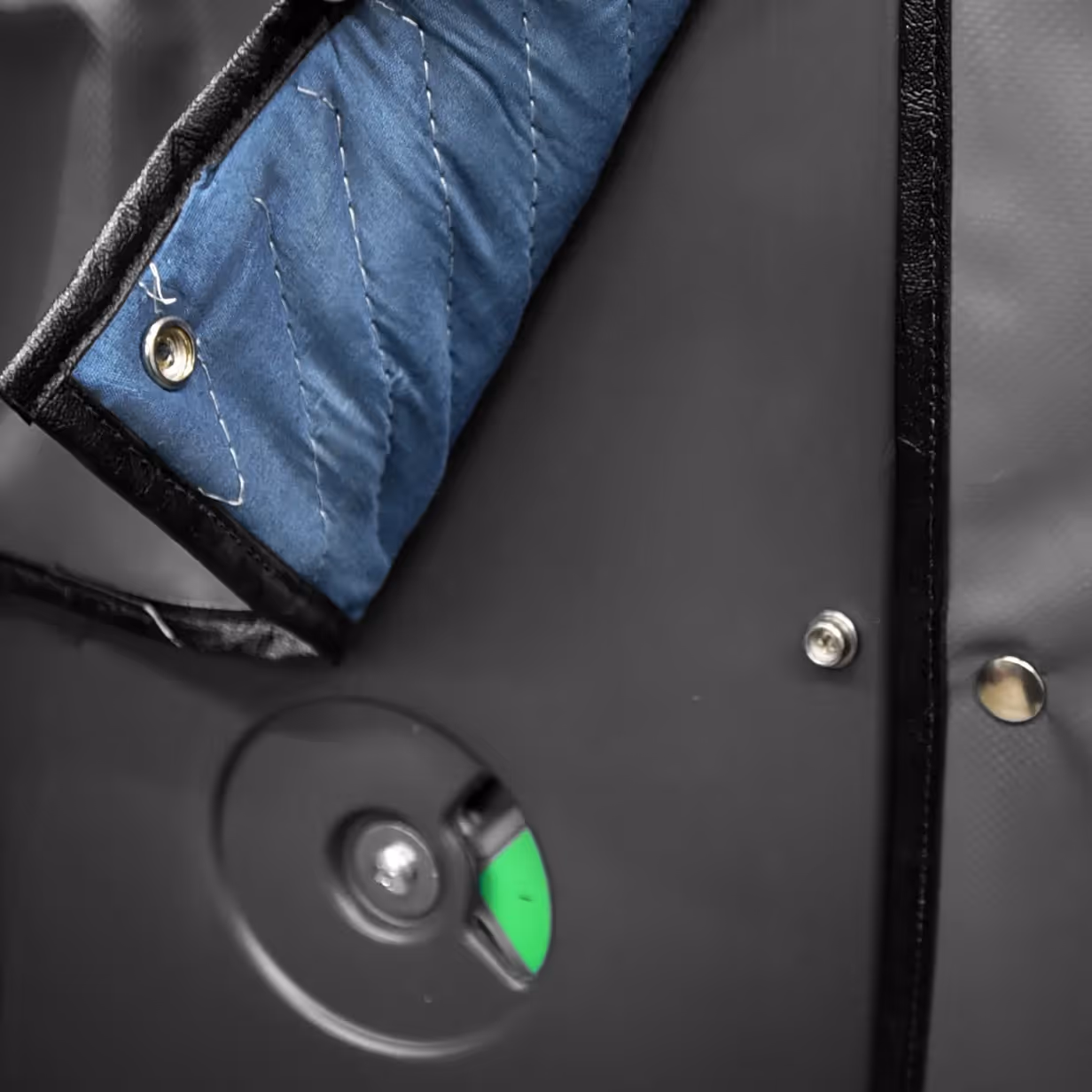 Close-up of insulated restroom cover with blue quilted fabric and black edging secured by metal rivets.