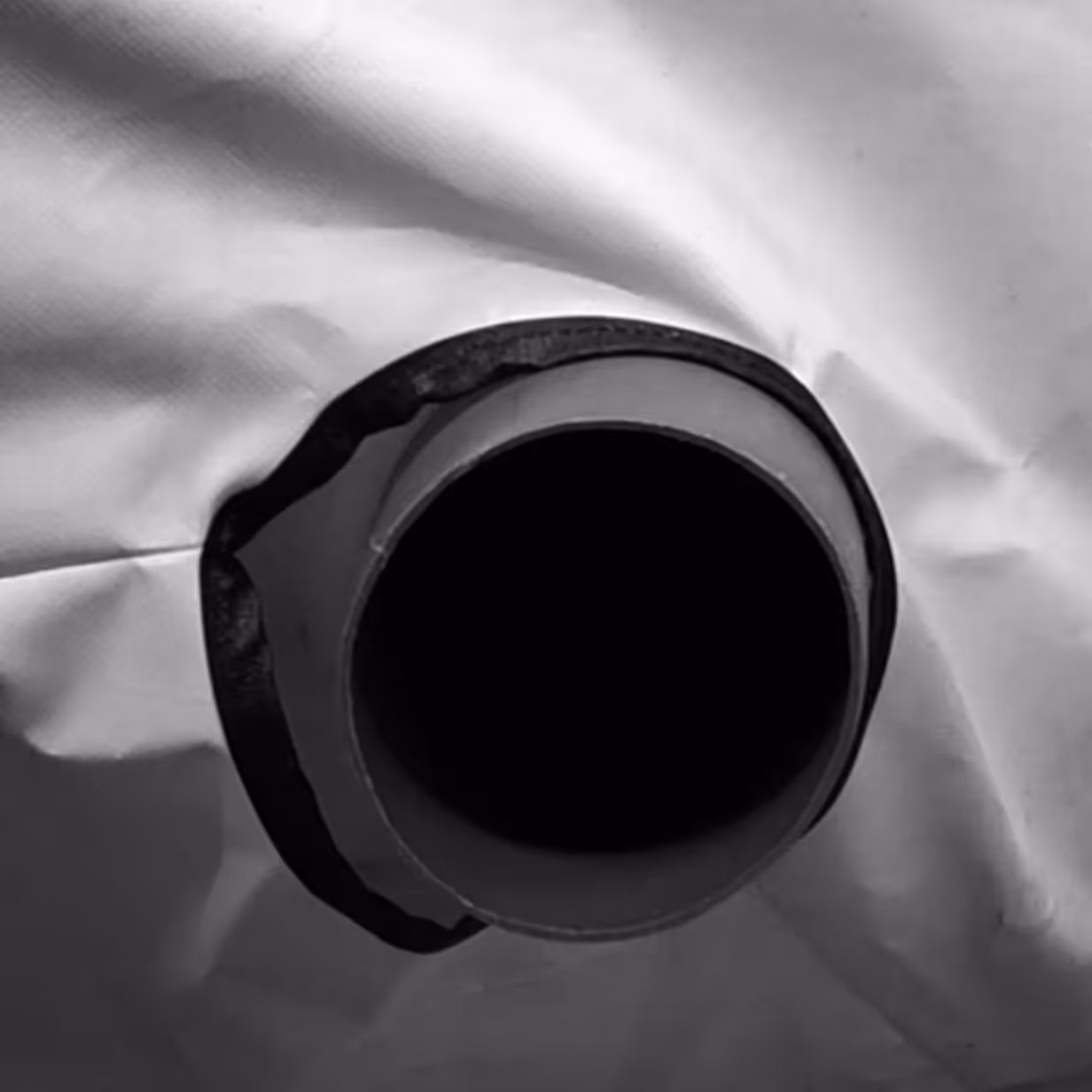 Close-up of a circular pipe opening surrounded by black sealing material on a white textured surface.