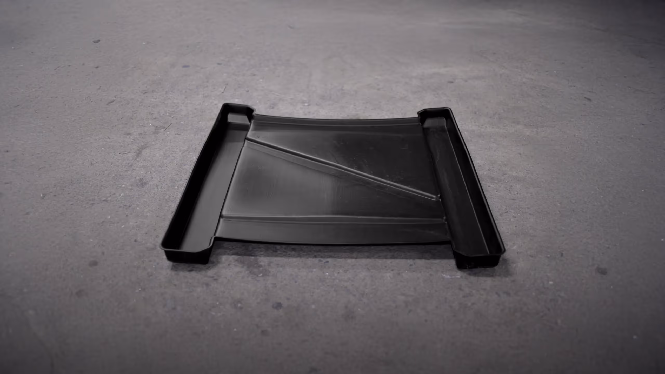 Black restroom containment tray with raised edges and a sloped design for liquid containment.