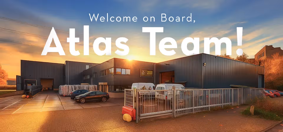 Modern industrial building at sunset with parked cars and text welcoming Atlas Team.