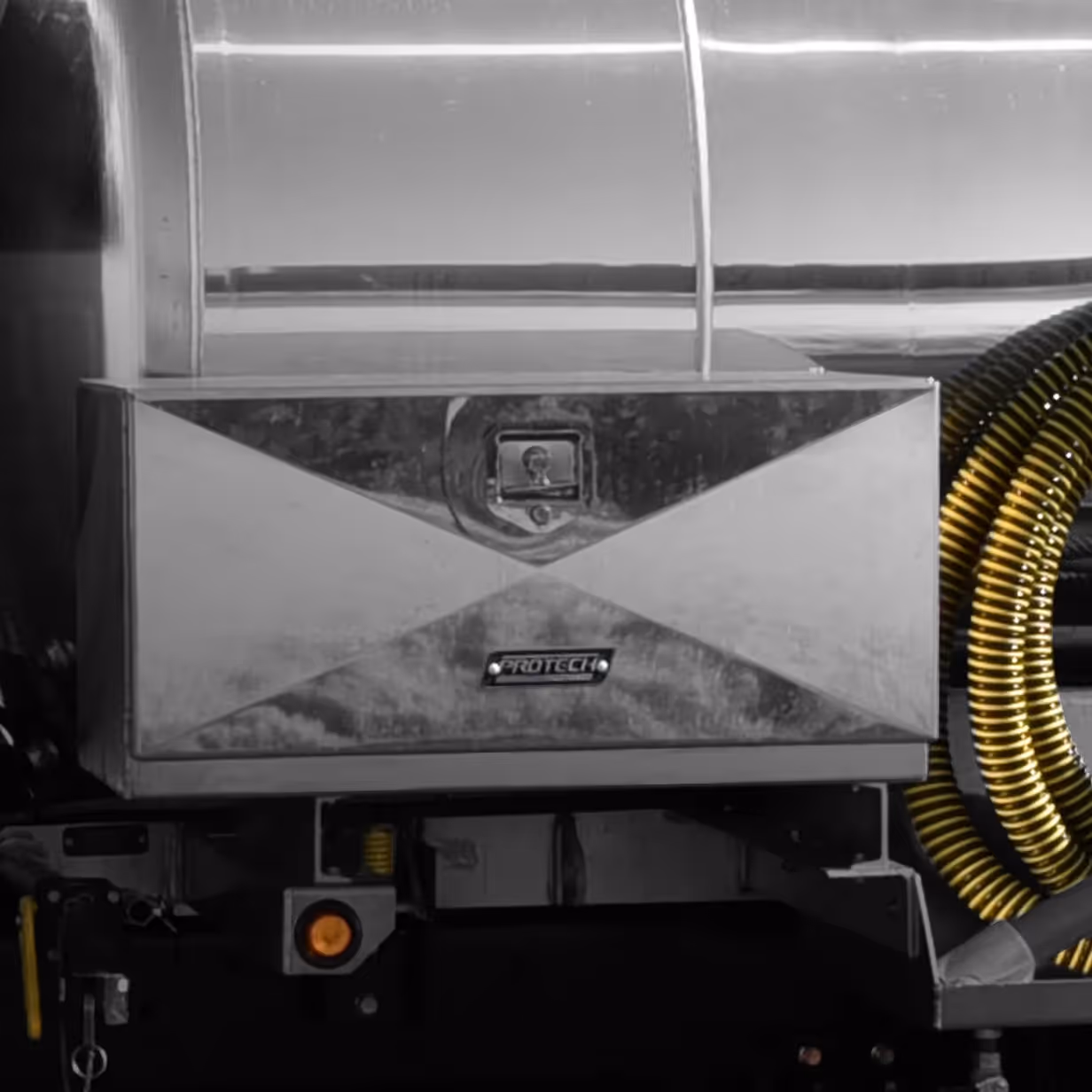 Rectangular silver metal toolbox with Protech logo mounted on vehicle with yellow coiled hose.