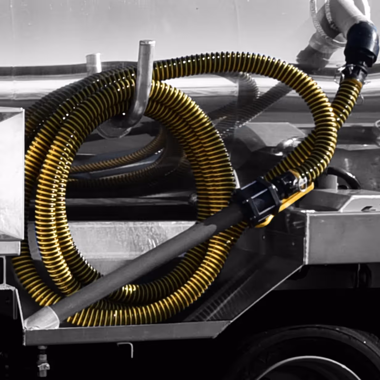 Yellow coiled industrial hose resting on a metal surface with equipment and a wheel below