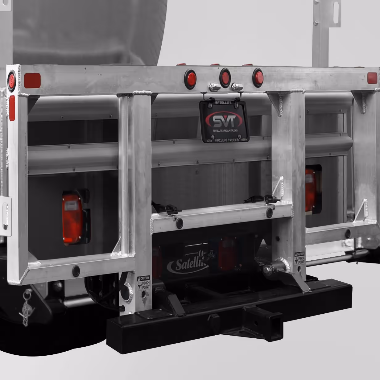 Rear metal frame of a truck with red lights, caution stickers, and a black bumper hitch.