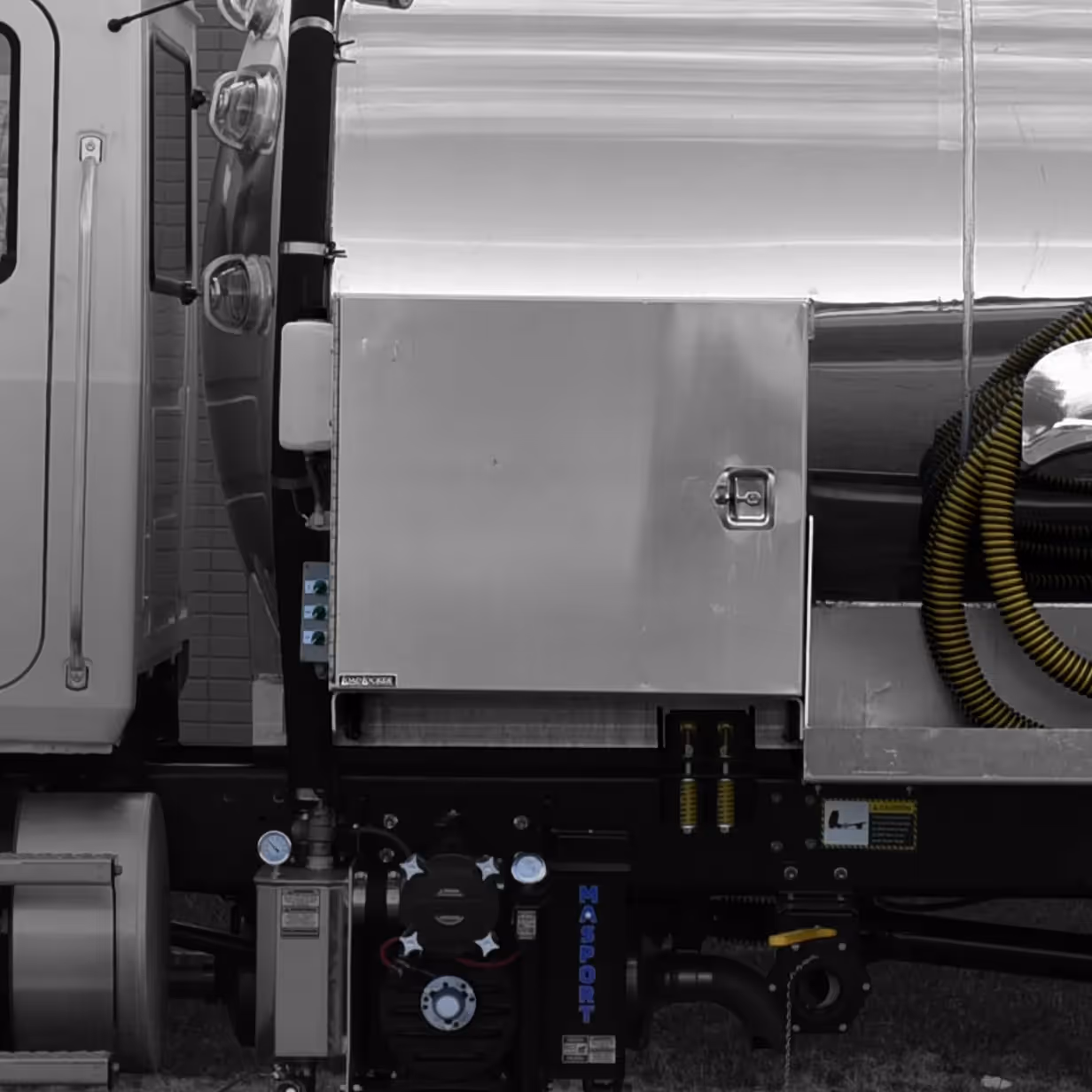 Close-up of a truck's aluminum cabinet and connected mechanical components with yellow coiled hoses.