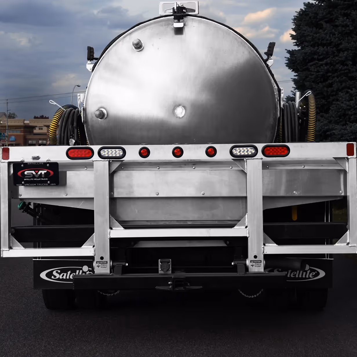 Rear view of a large silver industrial vacuum truck with hoses coiled on each side.