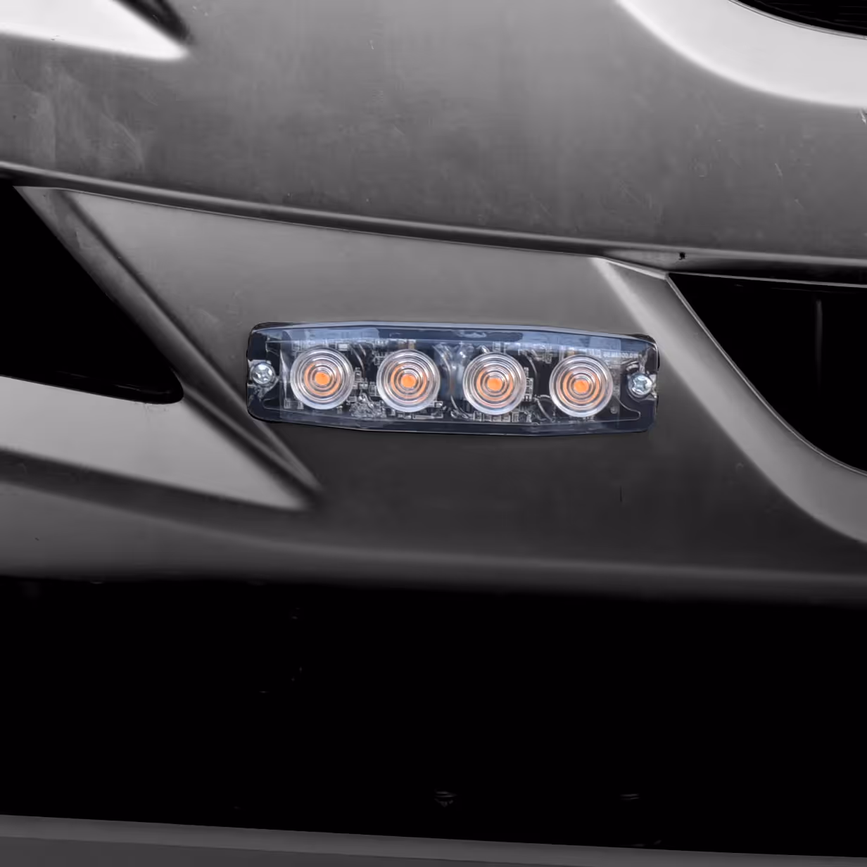 Close-up of a car bumper with four round orange LED lights mounted in a row.