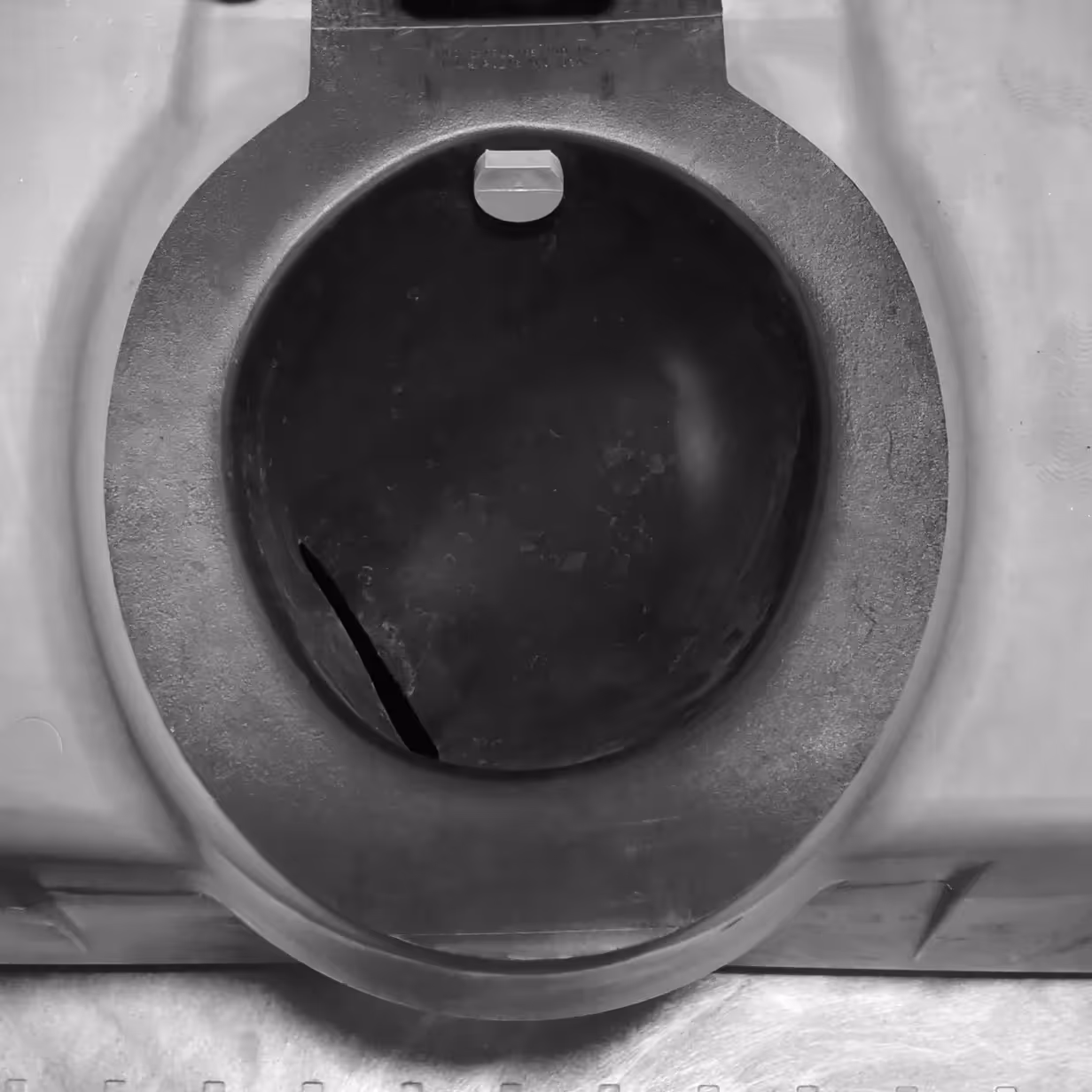 Top view of a round, cracked black rubber valve or seal inside a plastic housing.