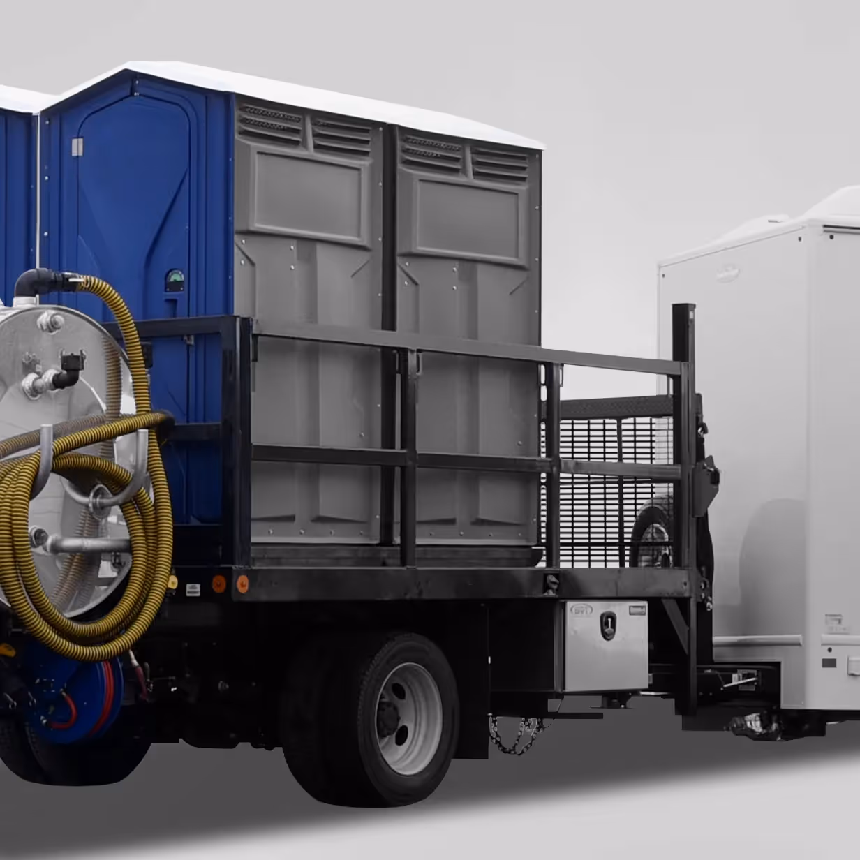 Truck bed loaded with two portable toilets and a large hose reel tank mounted on the side.
