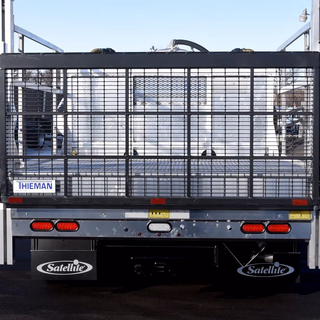 Rear view of a flatbed truck with a metal lift gate and red brake lights on a clear day.