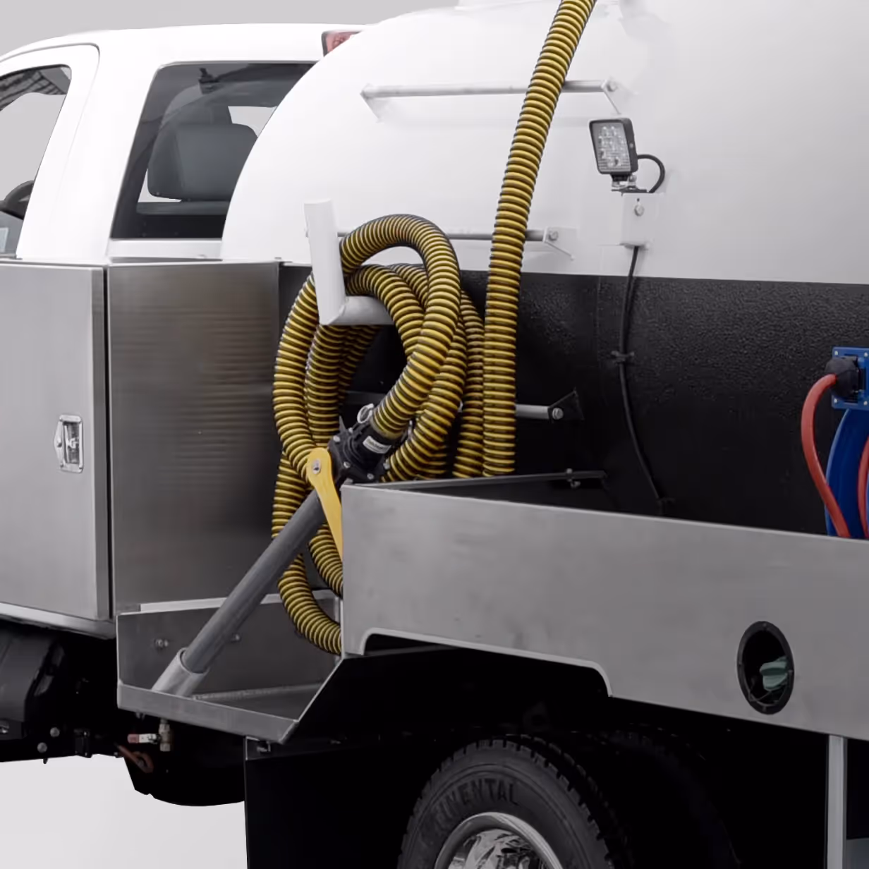 Yellow coiled hoses attached to a nozzle on the side of a white utility truck with stainless steel compartments.