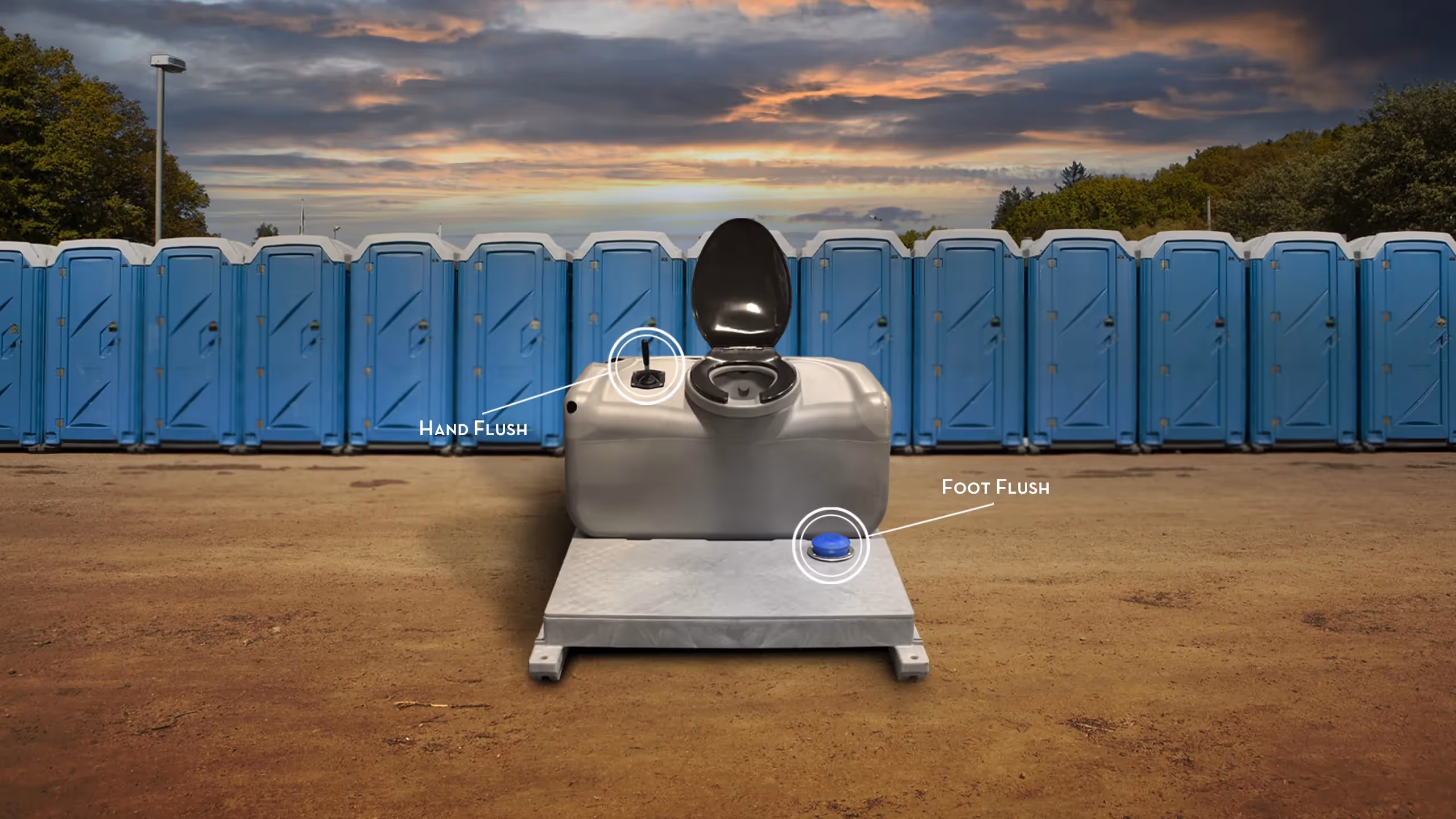 Portable toilet with black seat and hand and foot flush controls in front of blue porta-potties outdoors.