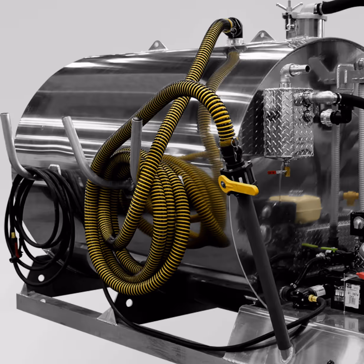 Yellow and black coiled hose mounted on a shiny metallic industrial tank with attached equipment.