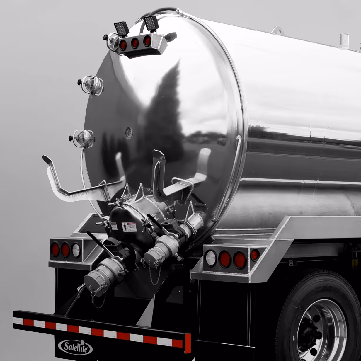 Rear view of a polished metal tanker truck with hose connections and red lights.