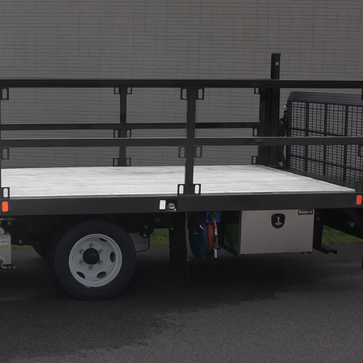 Side view of a flatbed truck with wooden bed and black metal rails parked on asphalt.
