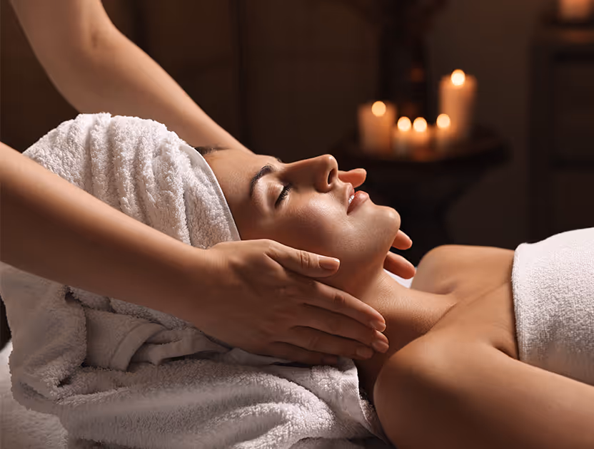 A woman receiving a facial massage in a serene spa setting, with candles in the background.
