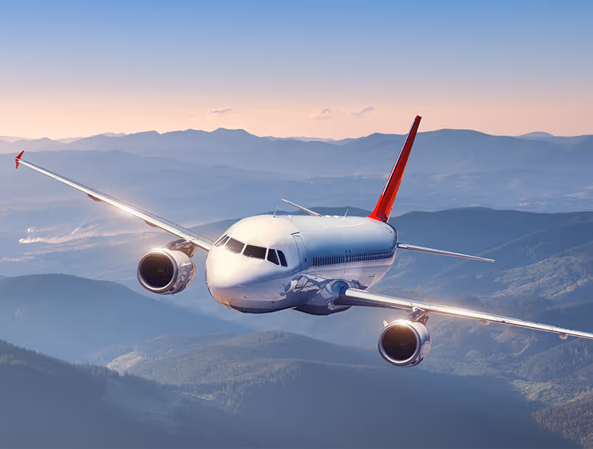 A commercial airplane flying over mountains during sunset with a clear sky.