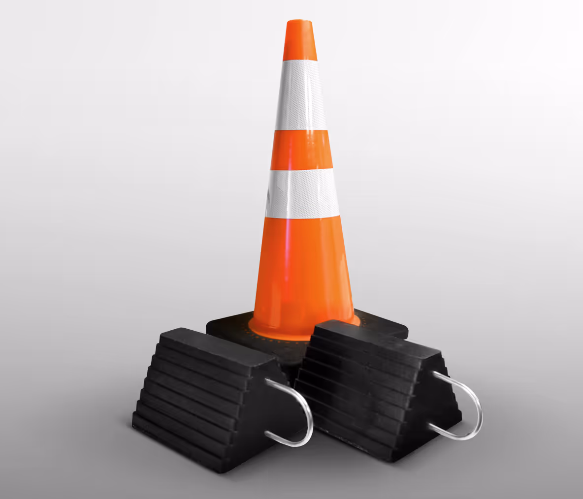 Orange traffic cone with white stripes, resting on two black rubber wheel chocks.