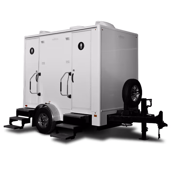 White portable restroom trailer with two doors and stairs, equipped with a spare tire on the side.
